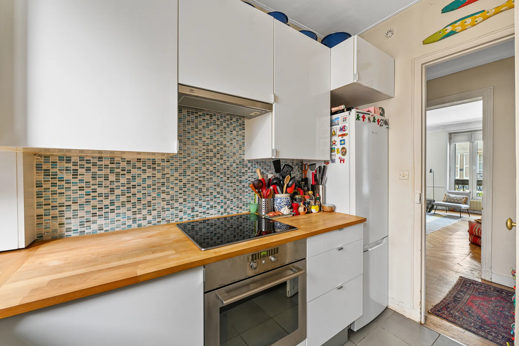 Una cocina compacta con gabinetes blancos, una encimera de madera y un salpicadero de azulejos.