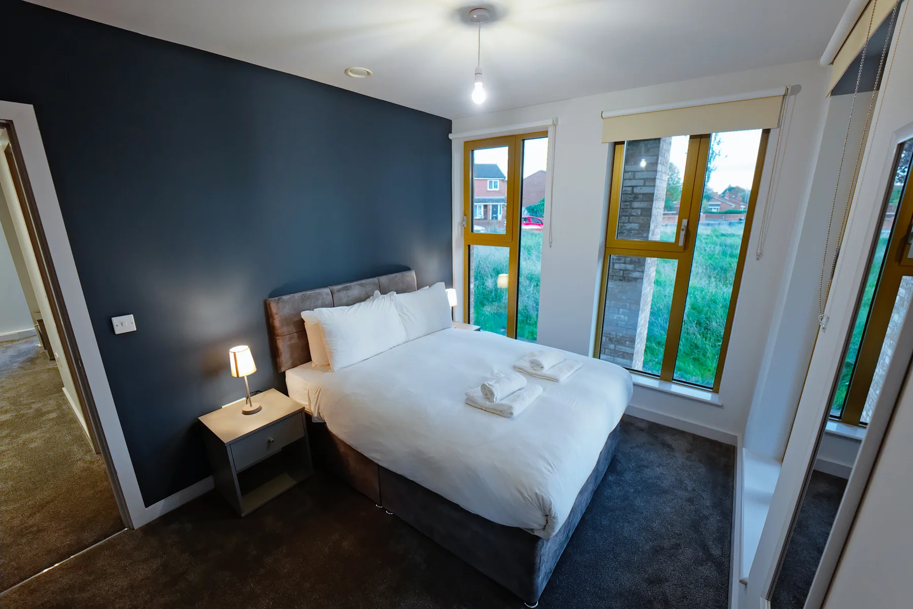 A bedroom with a bed dressed in white linens beside tall windows.