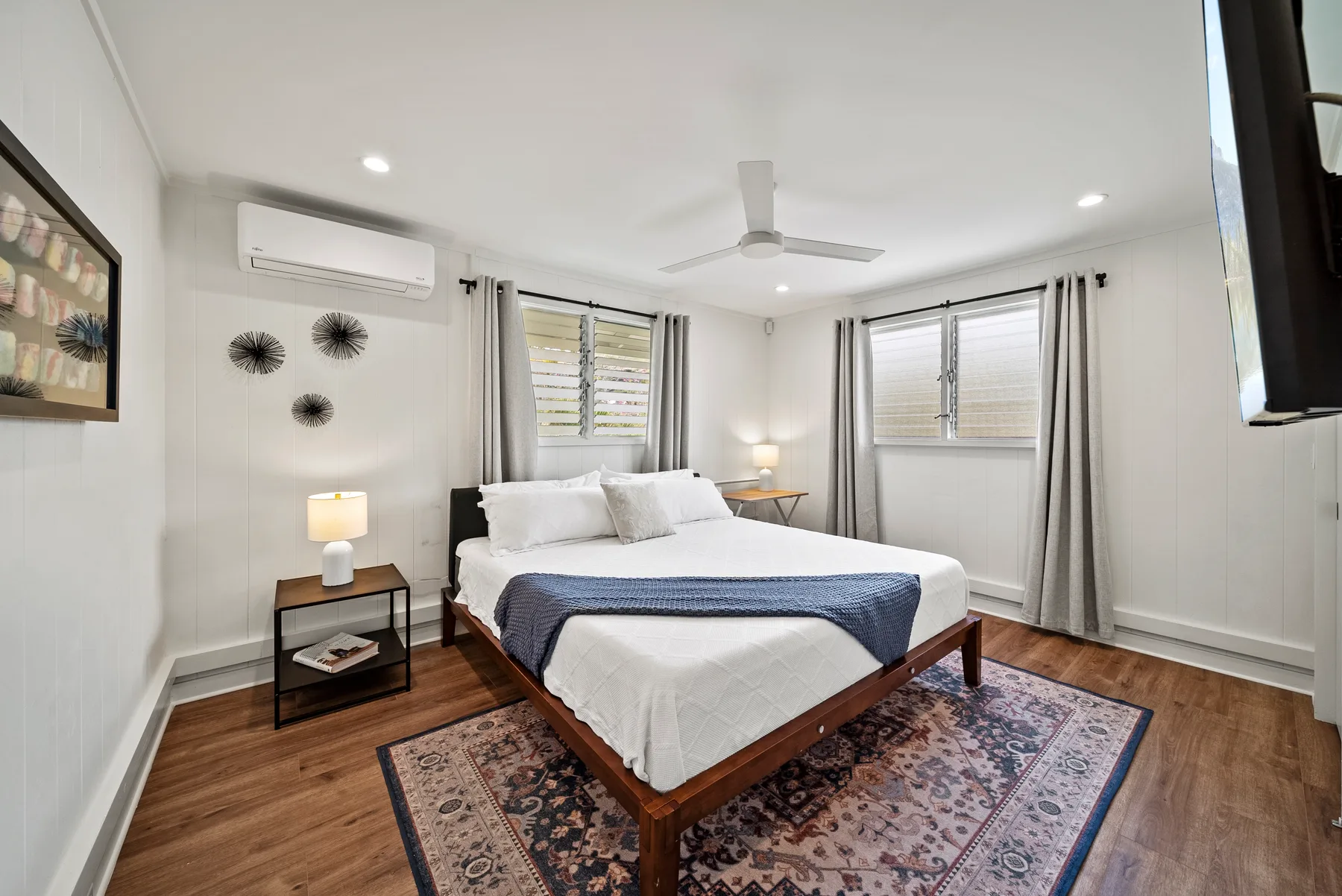 Un dormitorio luminoso con una cama grande, una alfombra estampada y ventanas.