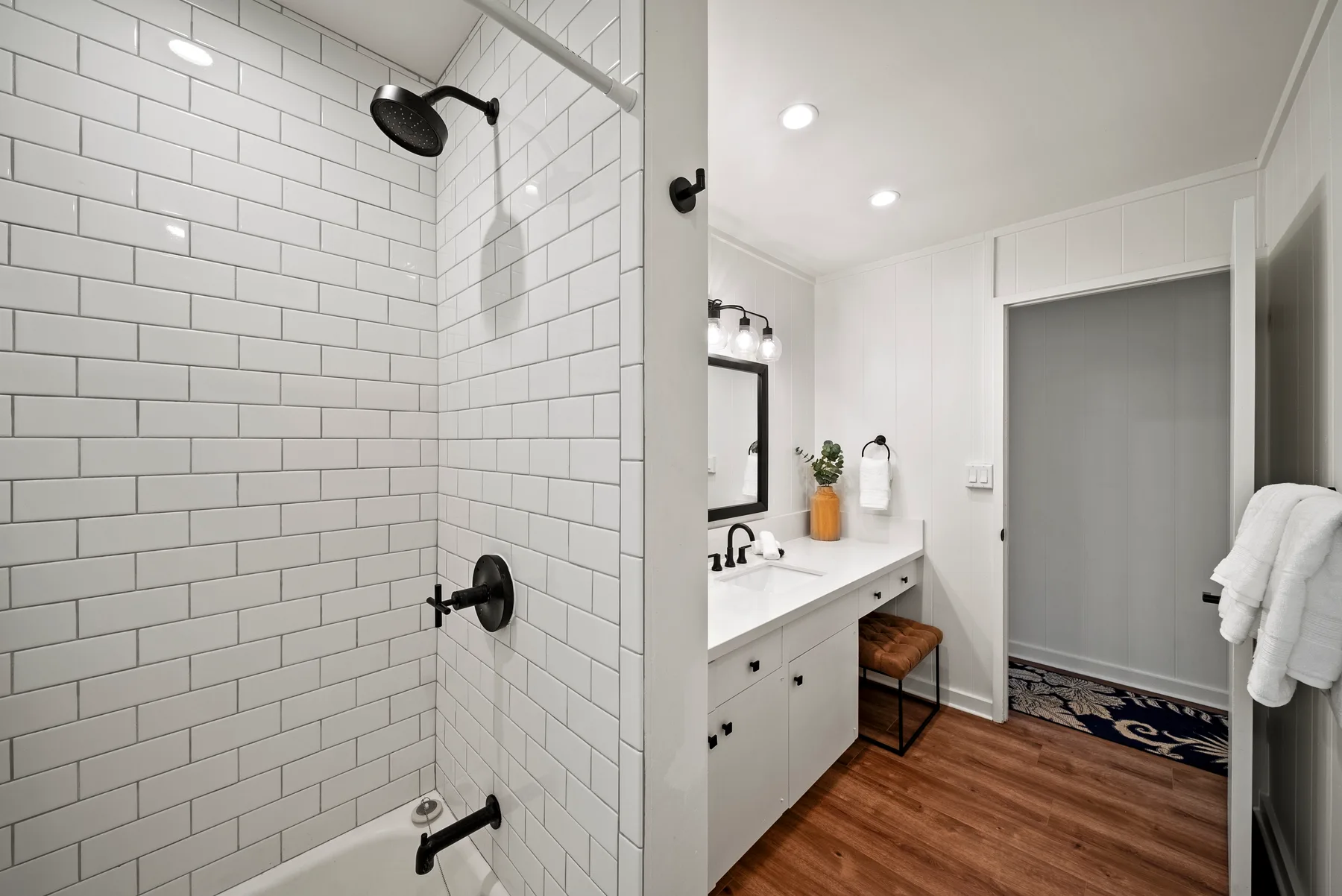 Un baño con ducha de azulejos, lavabo y suelo de aspecto madera.