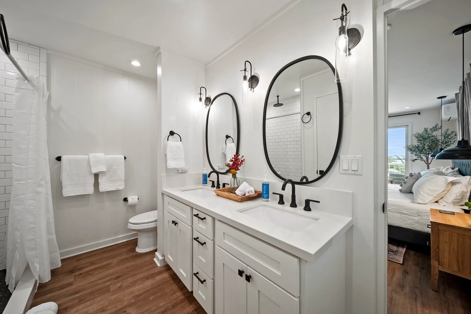 Un baño luminoso con lavabo doble, espejos ovalados y una zona de bañera y ducha.
