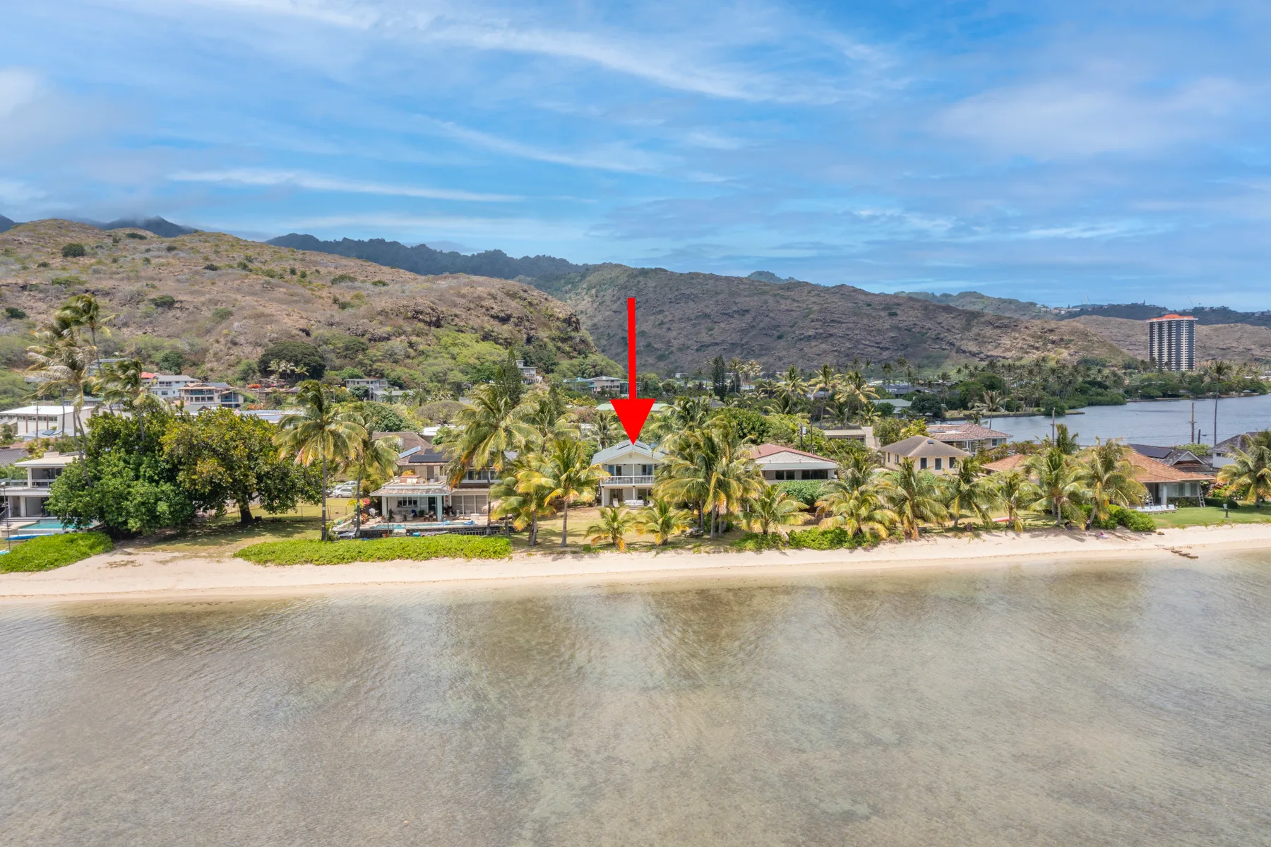 Vista aérea de una orilla arenosa, palmeras y casas bajo colinas áridas.