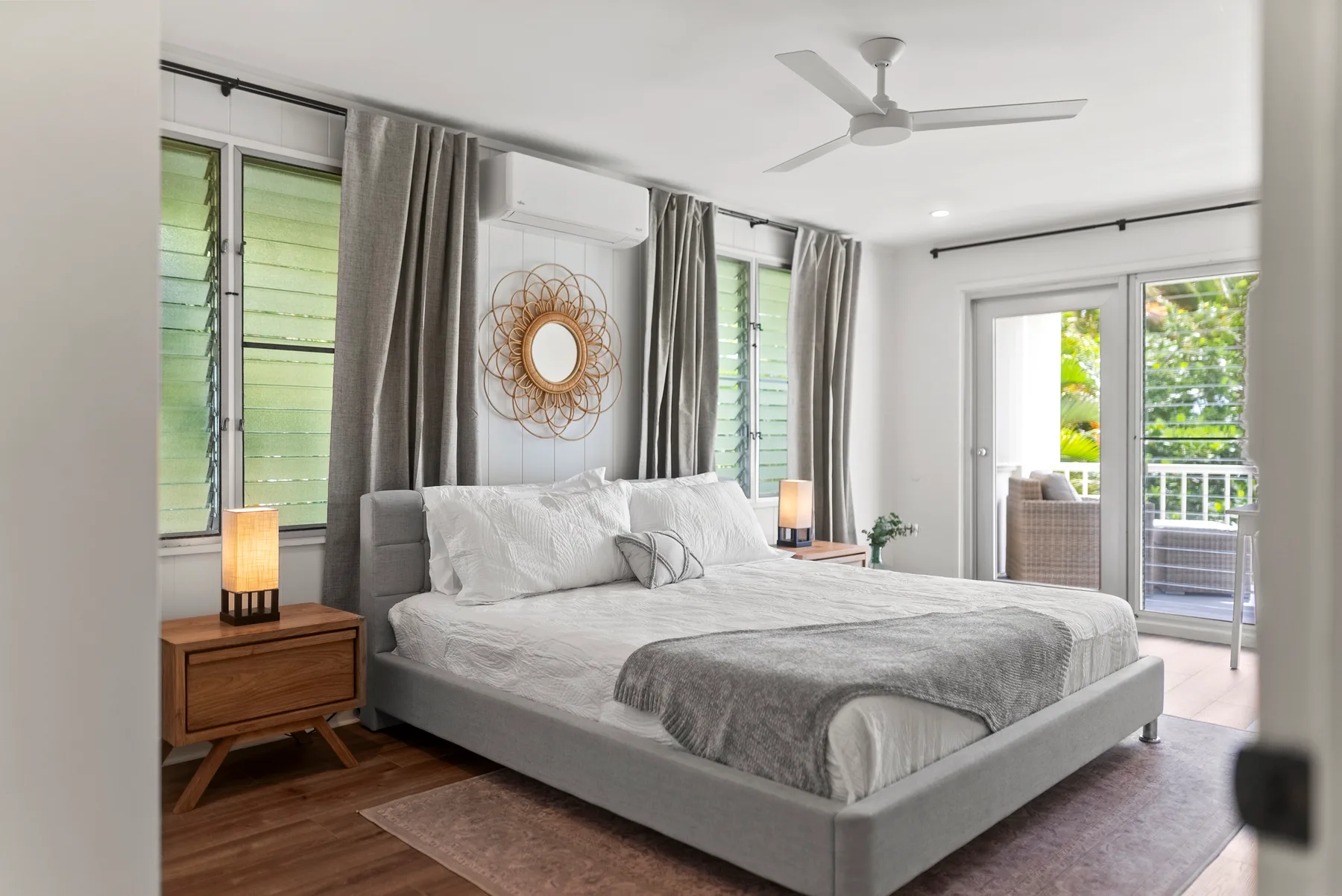 Un dormitorio luminoso con una cama grande, cortinas grises y ventanas que dan a un balcón.