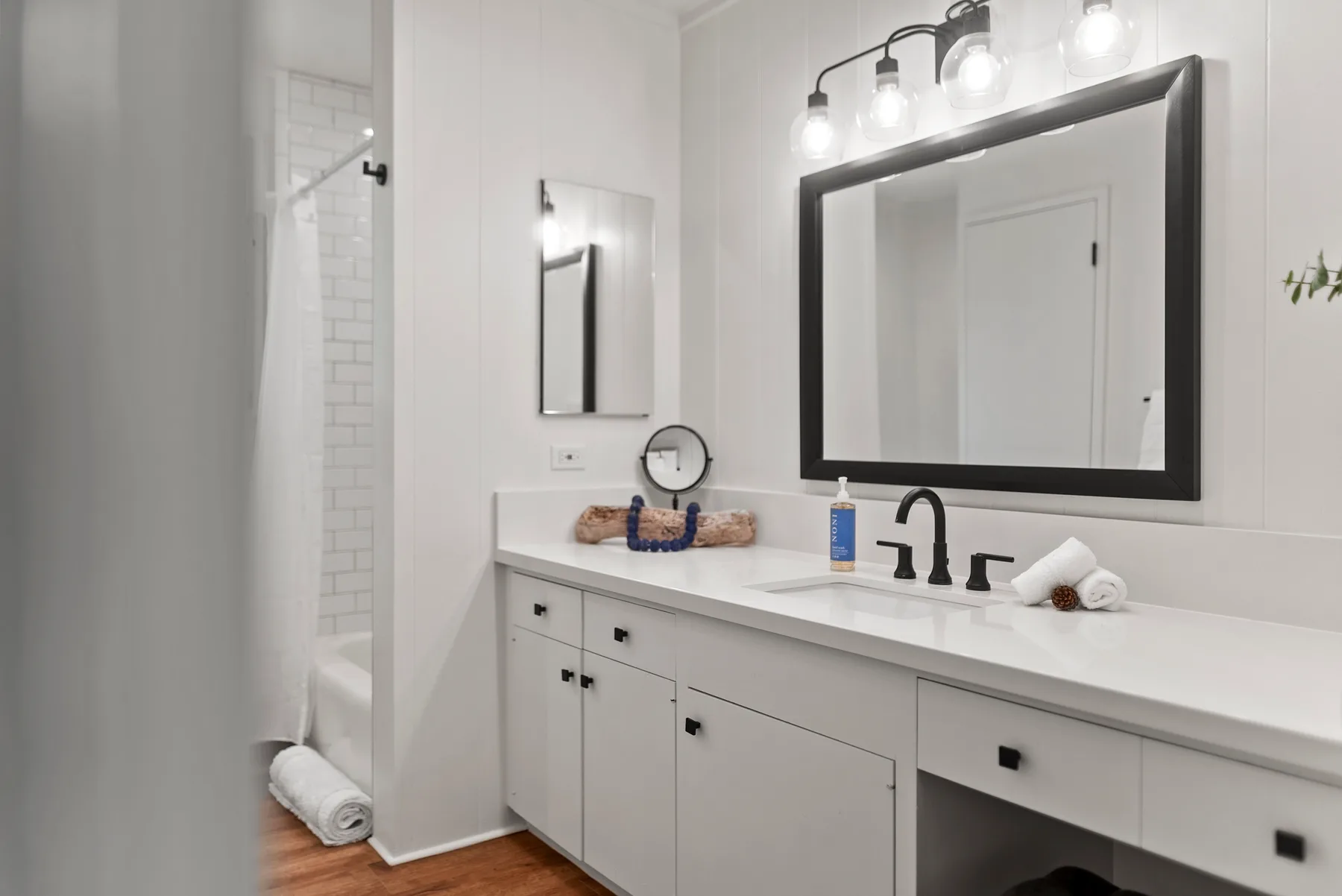 Un lavabo de baño luminoso con un espejo grande y una zona de ducha.