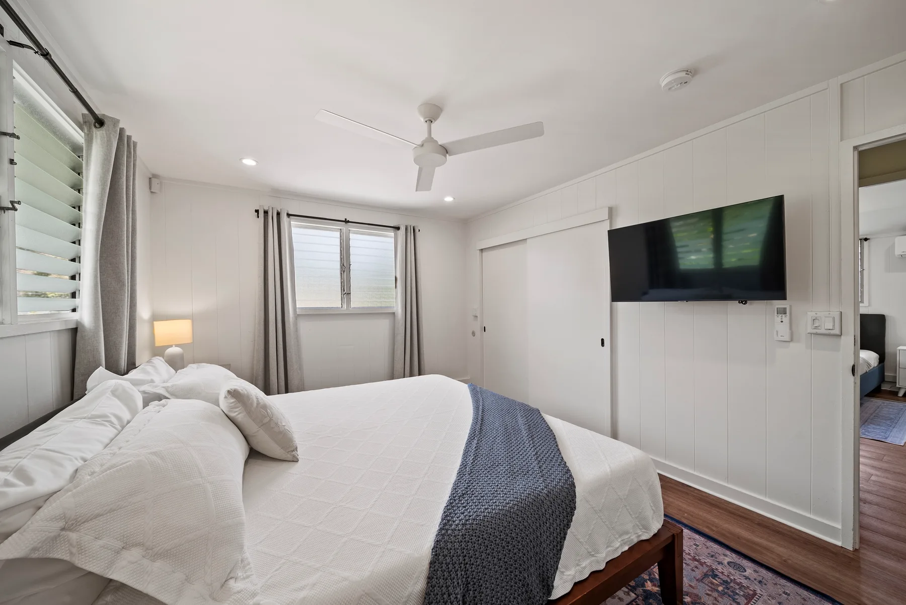 Un dormitorio con la cama tendida, un ventilador de techo y un televisor en la pared.