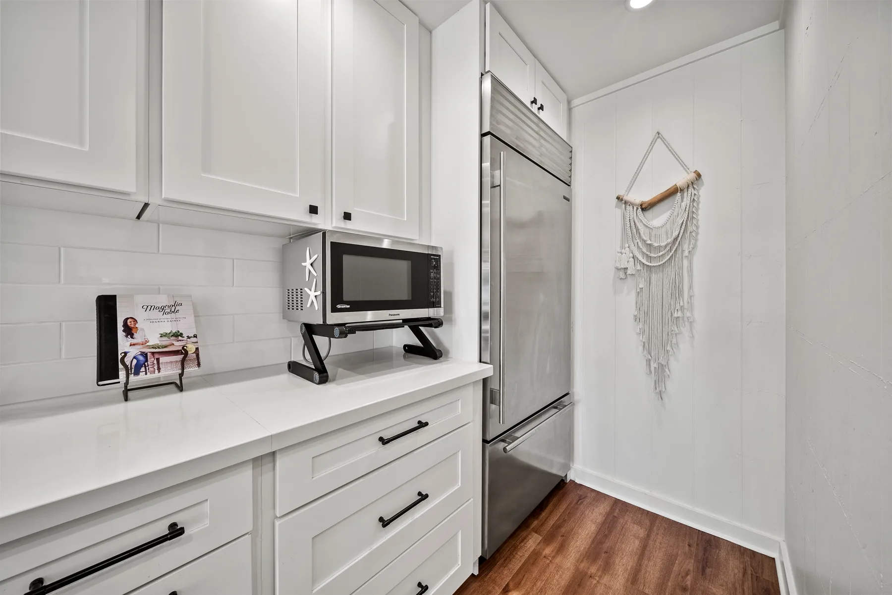 Una cocina luminosa con gabinetes blancos, un microondas y un refrigerador de acero inoxidable.