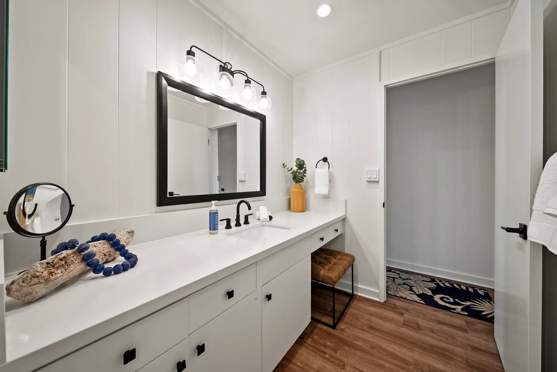 Una luminosa zona de lavabo con un espejo grande y una puerta hacia una ducha con azulejos.