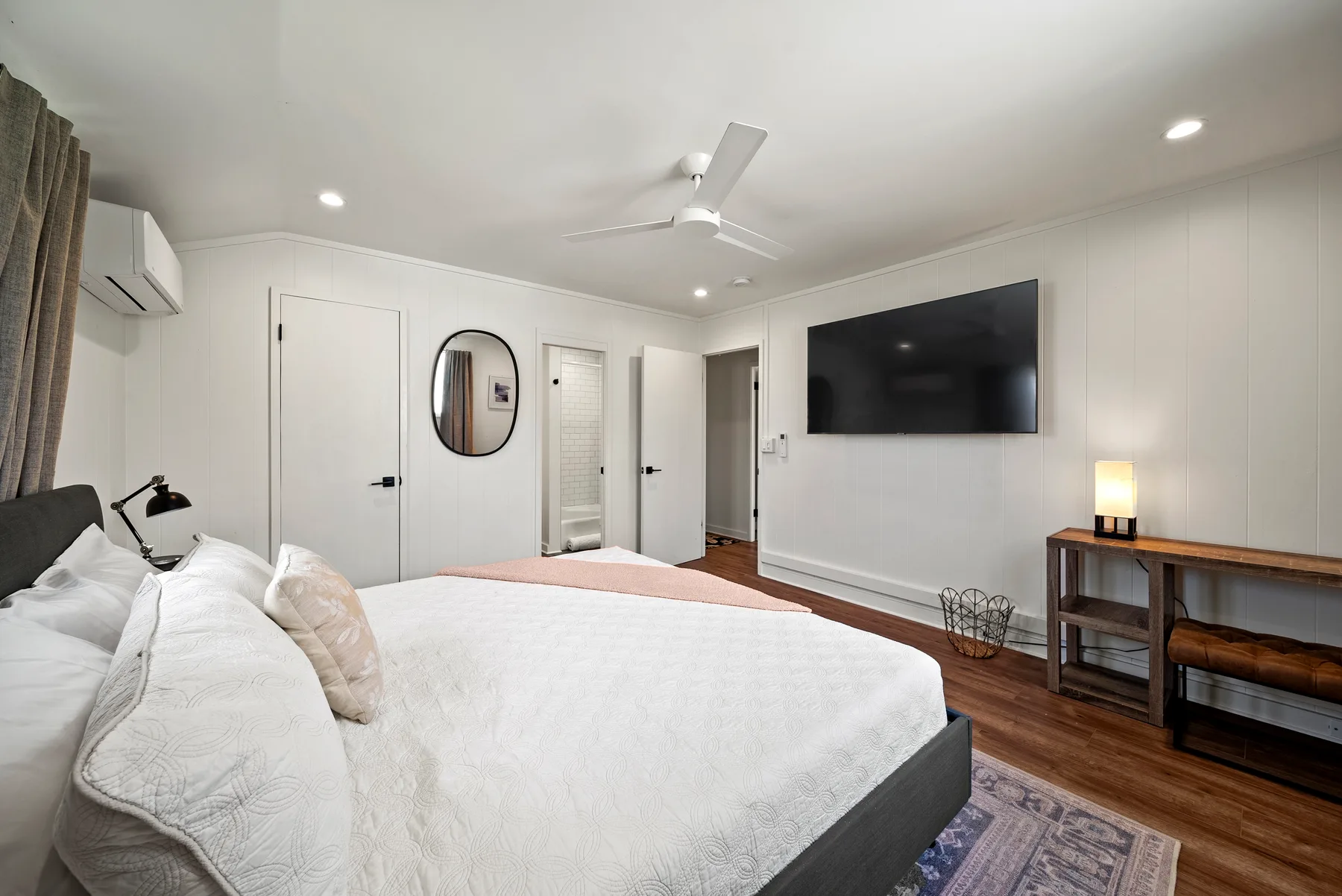 Un dormitorio luminoso con una cama grande y un televisor montado en la pared.