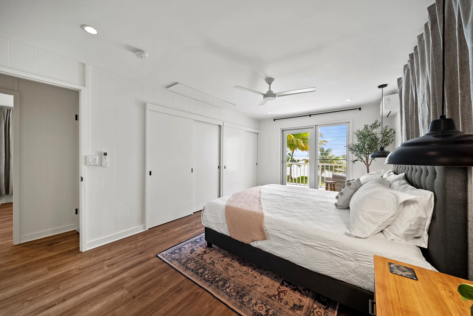 Un dormitorio luminoso con una cama, suelo de madera y puertas de vidrio que dan a un balcón.