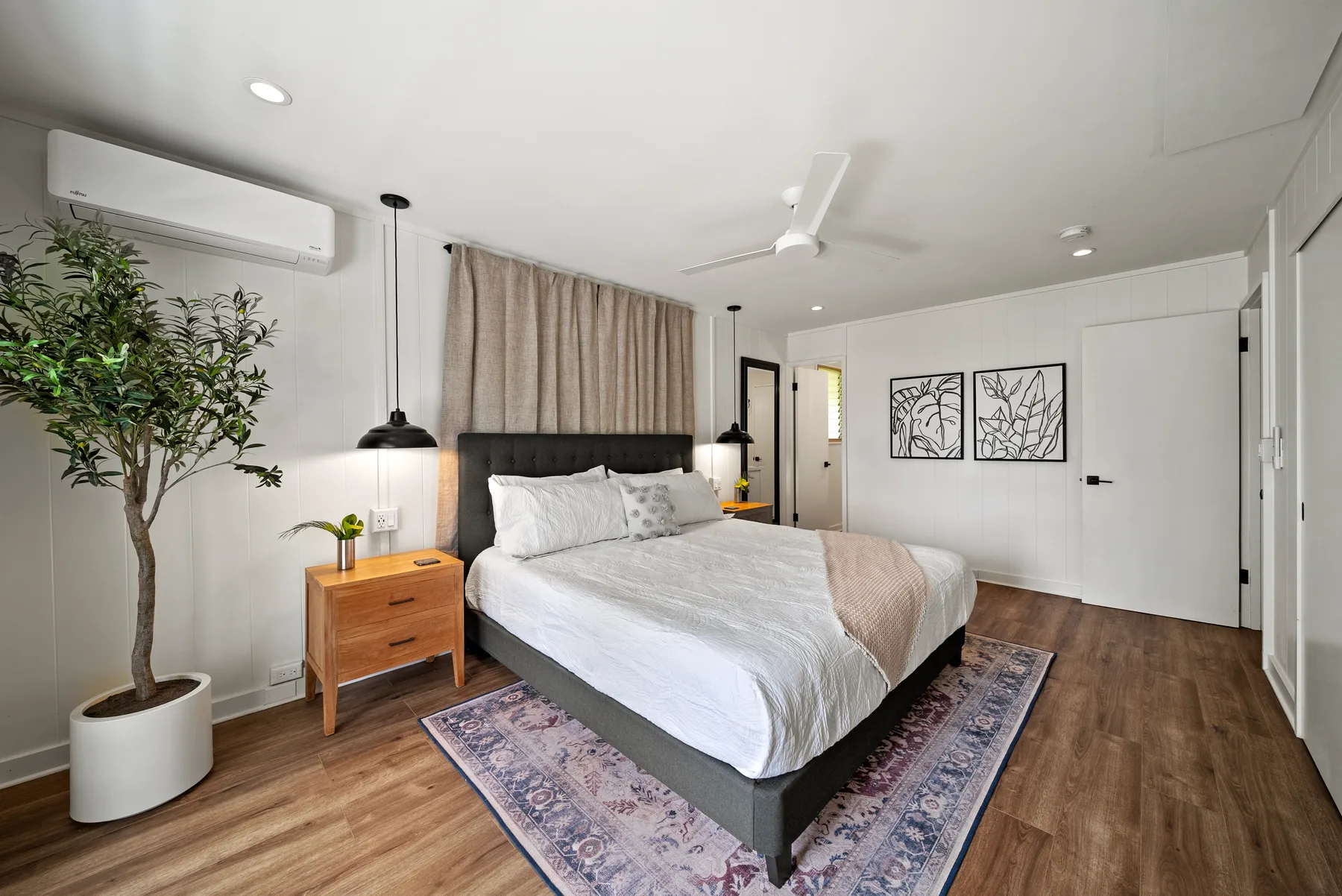 Un dormitorio luminoso con una cama, una mesita de noche y un árbol en maceta.