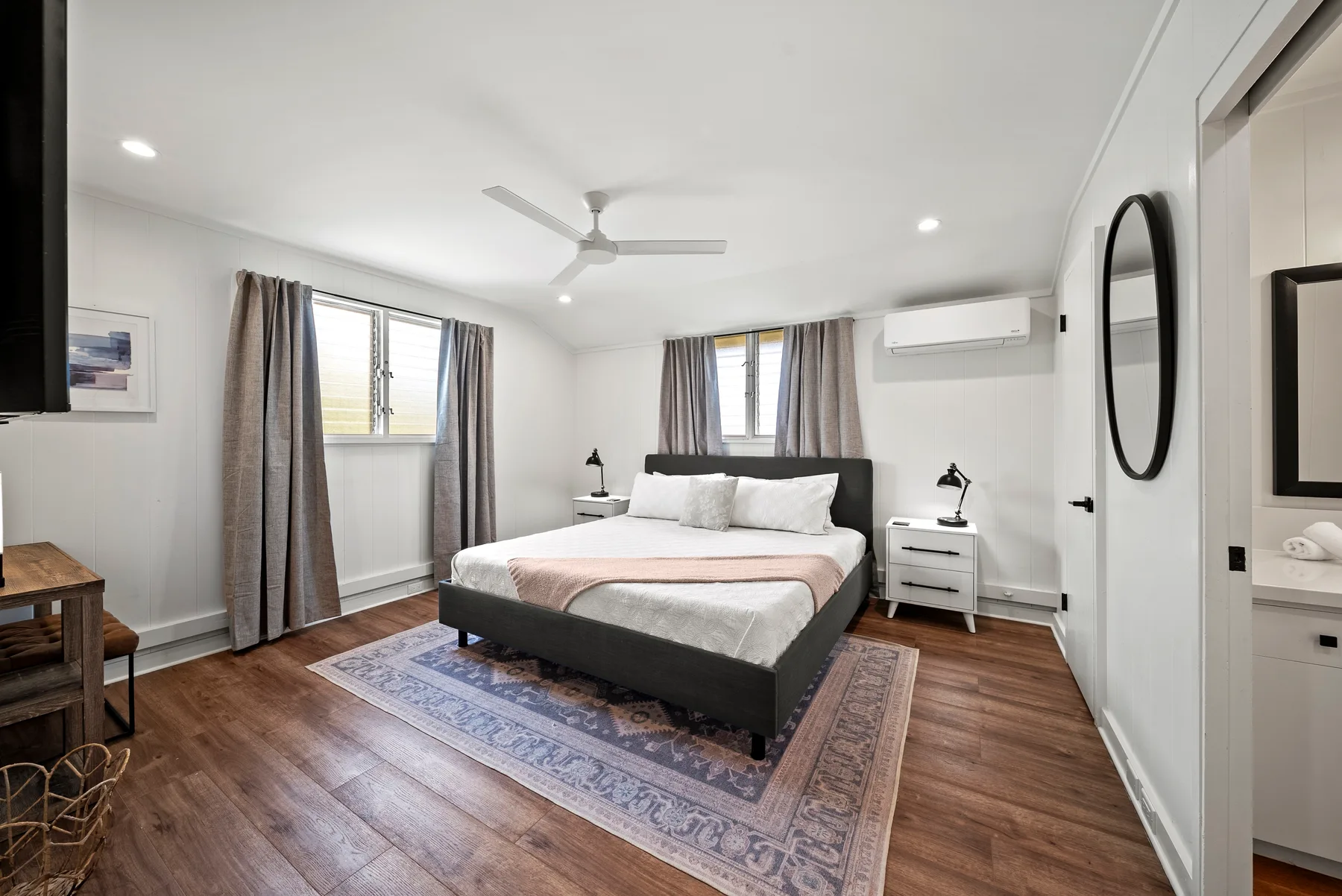 Un dormitorio con una cama sobre una alfombra estampada y ventanas con cortinas.