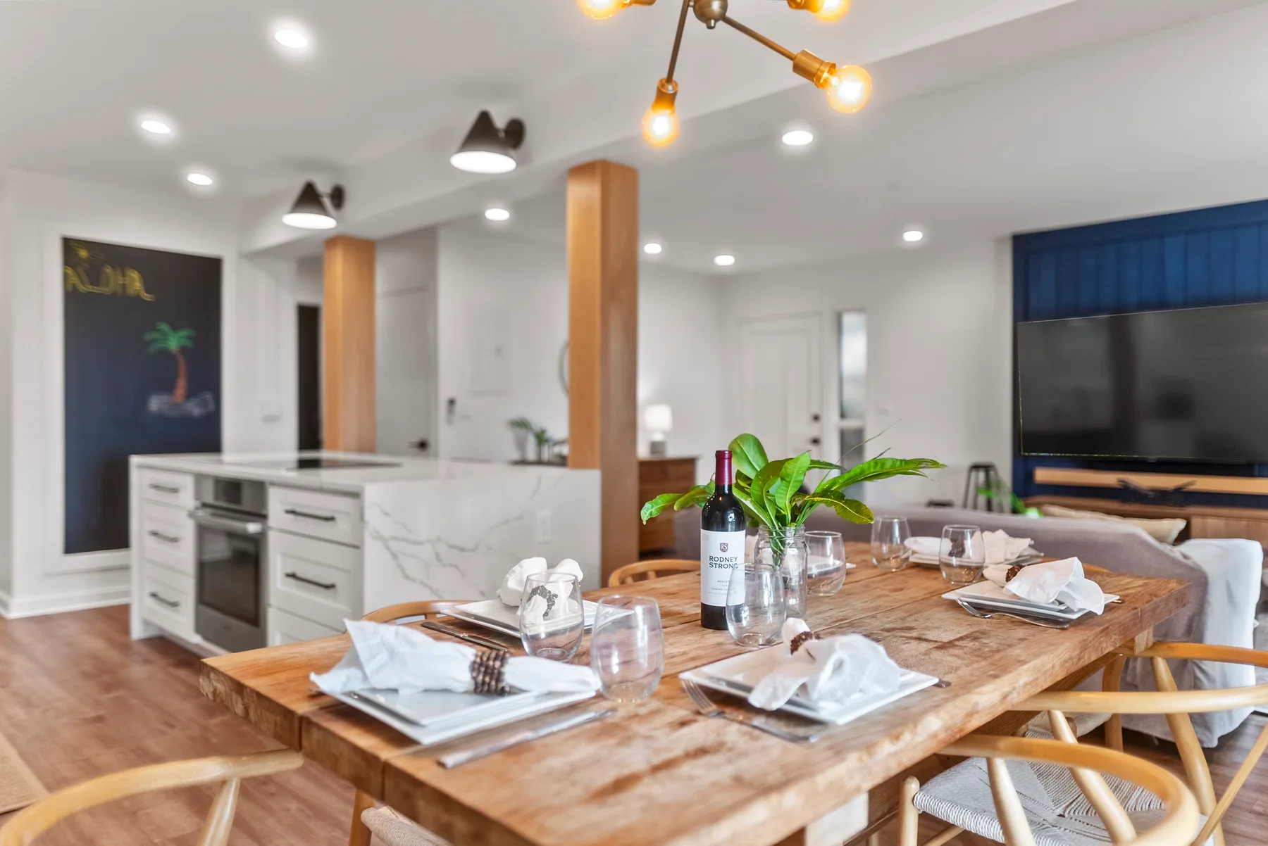 Un comedor con una mesa de madera preparada y una cocina abierta al fondo.