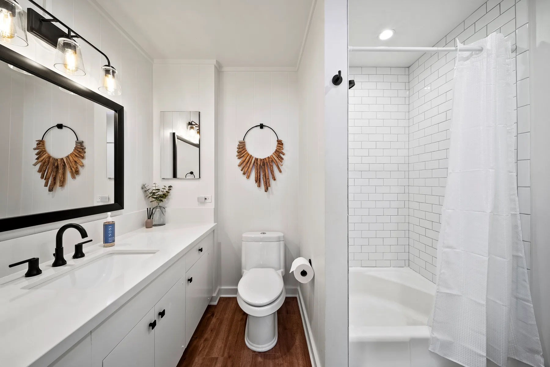 Un baño luminoso con un tocador largo y una ducha con azulejos.