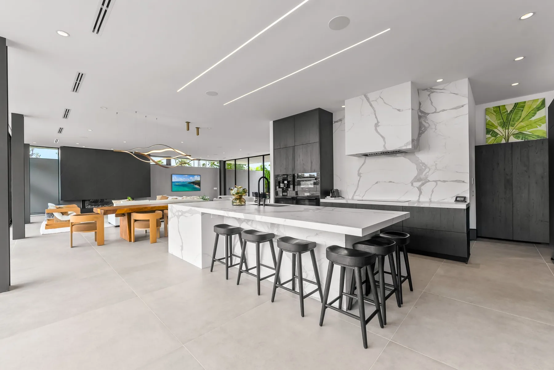 A modern kitchen with a long island and stools opens onto a dining area.