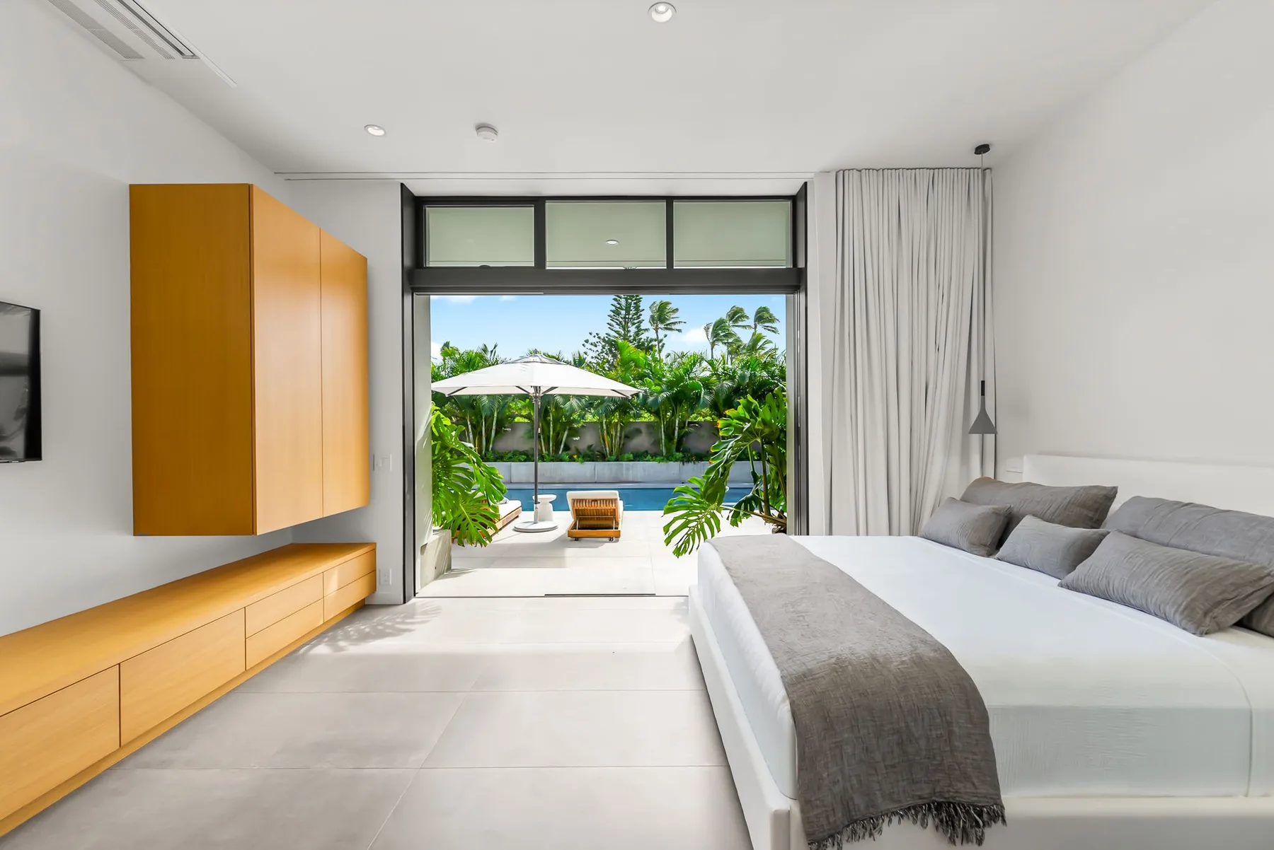 A bright bedroom opens onto a patio with a pool and greenery.