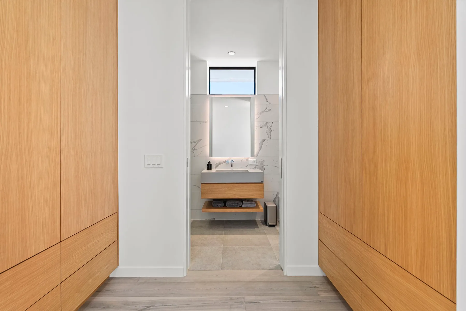 A hallway opens onto a bathroom with a floating vanity and mirror.