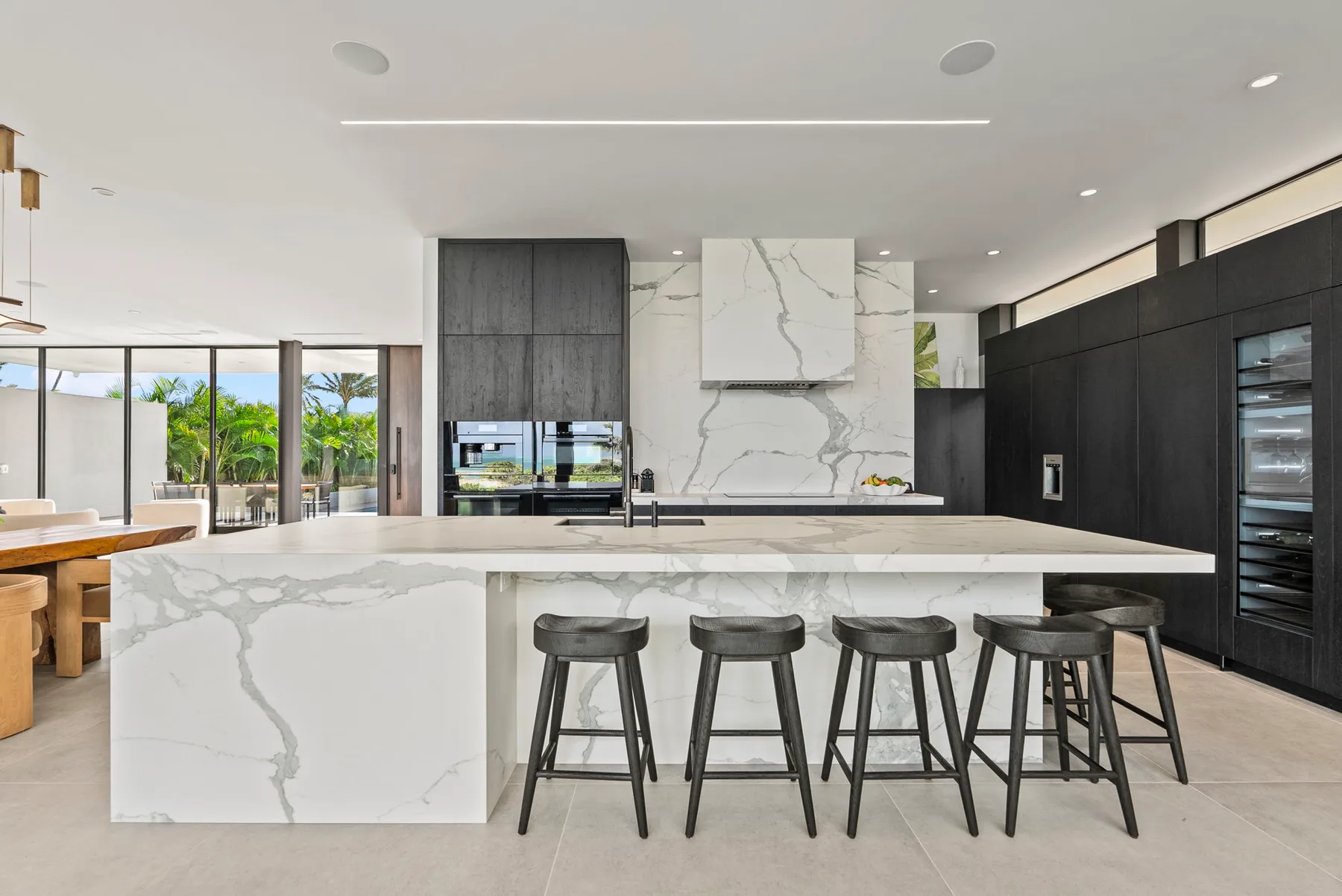A modern kitchen with a large island and seating, opening onto a dining area.