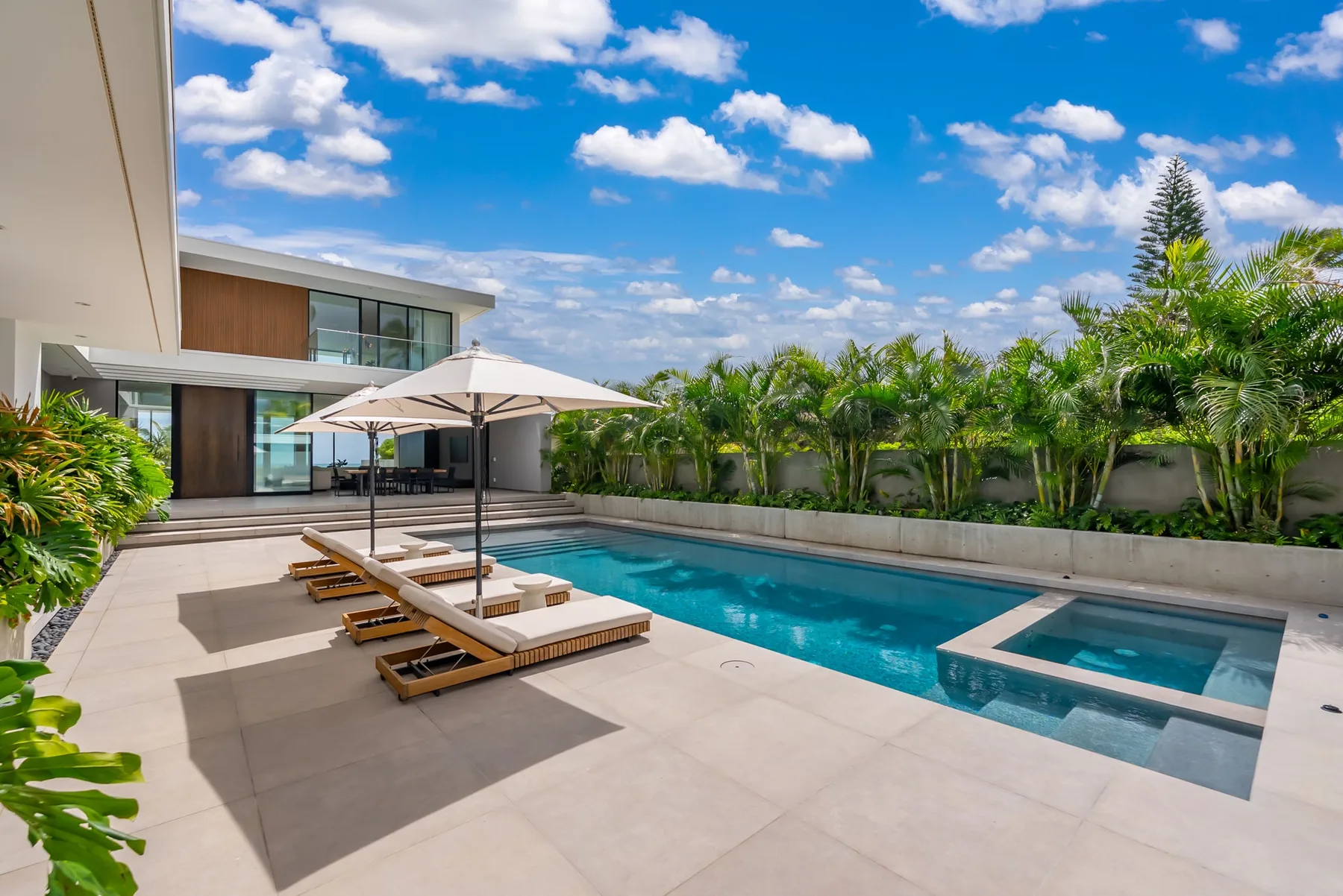 A sunny outdoor poolside patio with lounge seating and a landscaped border.