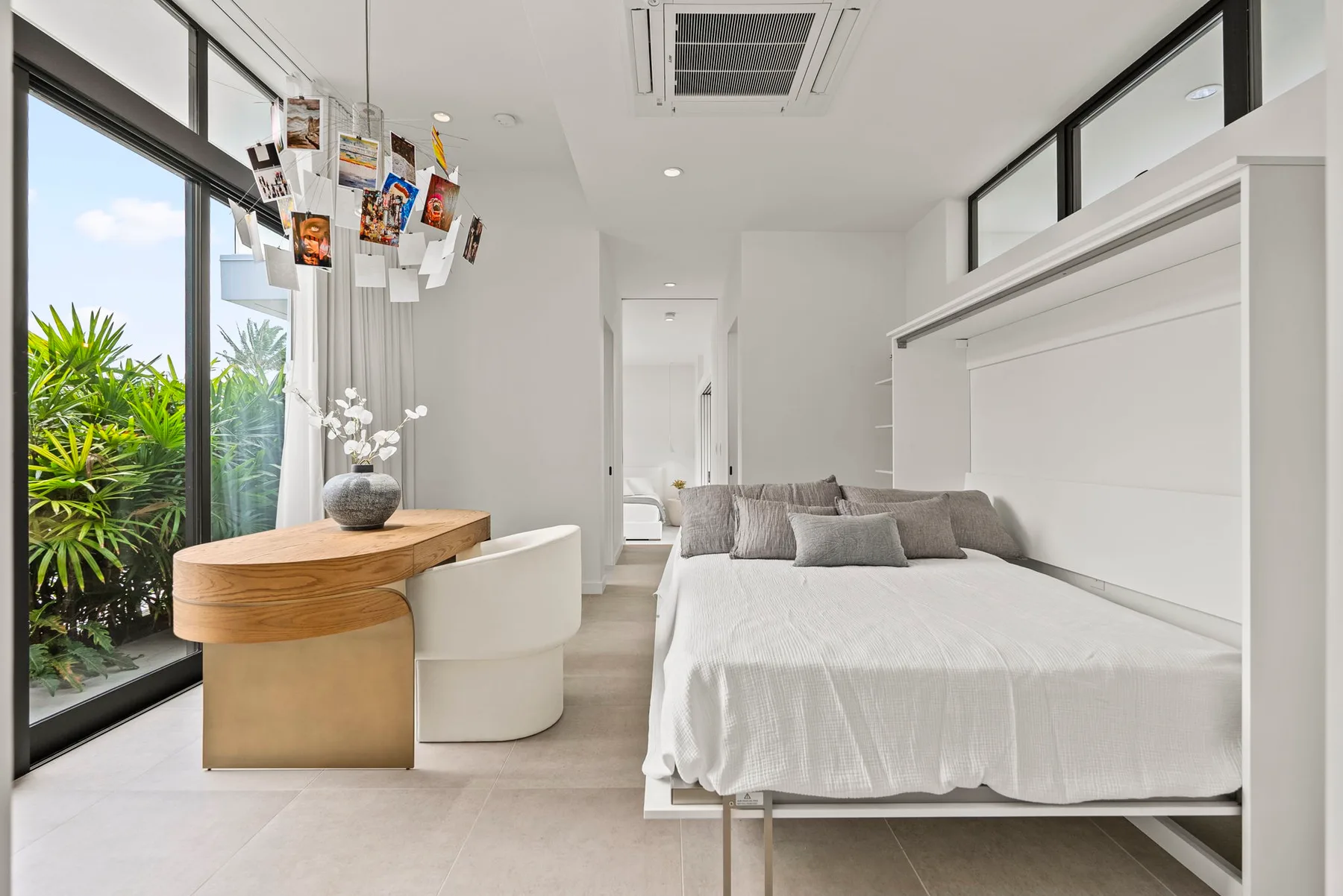 A bright bedroom with a large bed and a desk beside floor-to-ceiling windows.