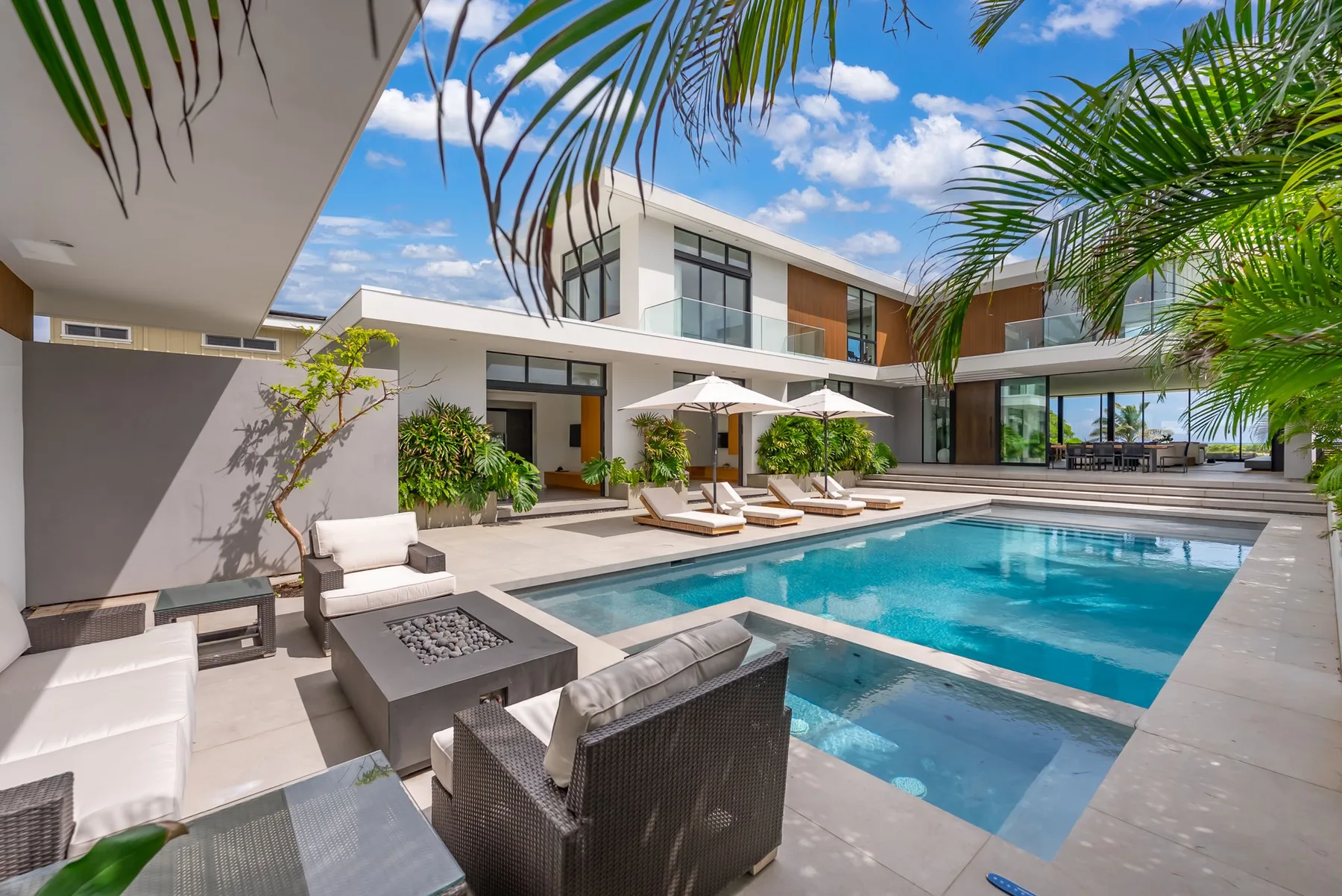A courtyard pool beside a modern house, with lounge seating and palm trees.