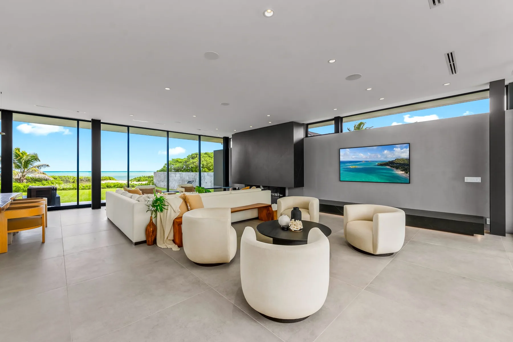 A spacious living room with white seating and large windows overlooking the ocean.