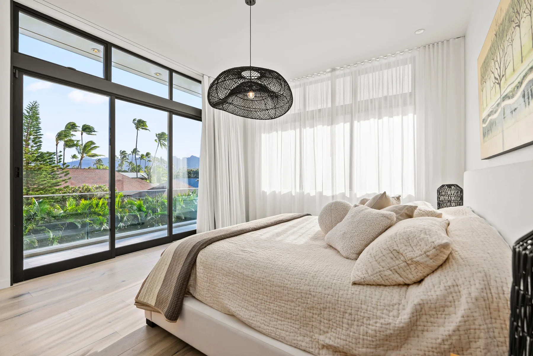 A bright bedroom with a bed beside large windows overlooking greenery.