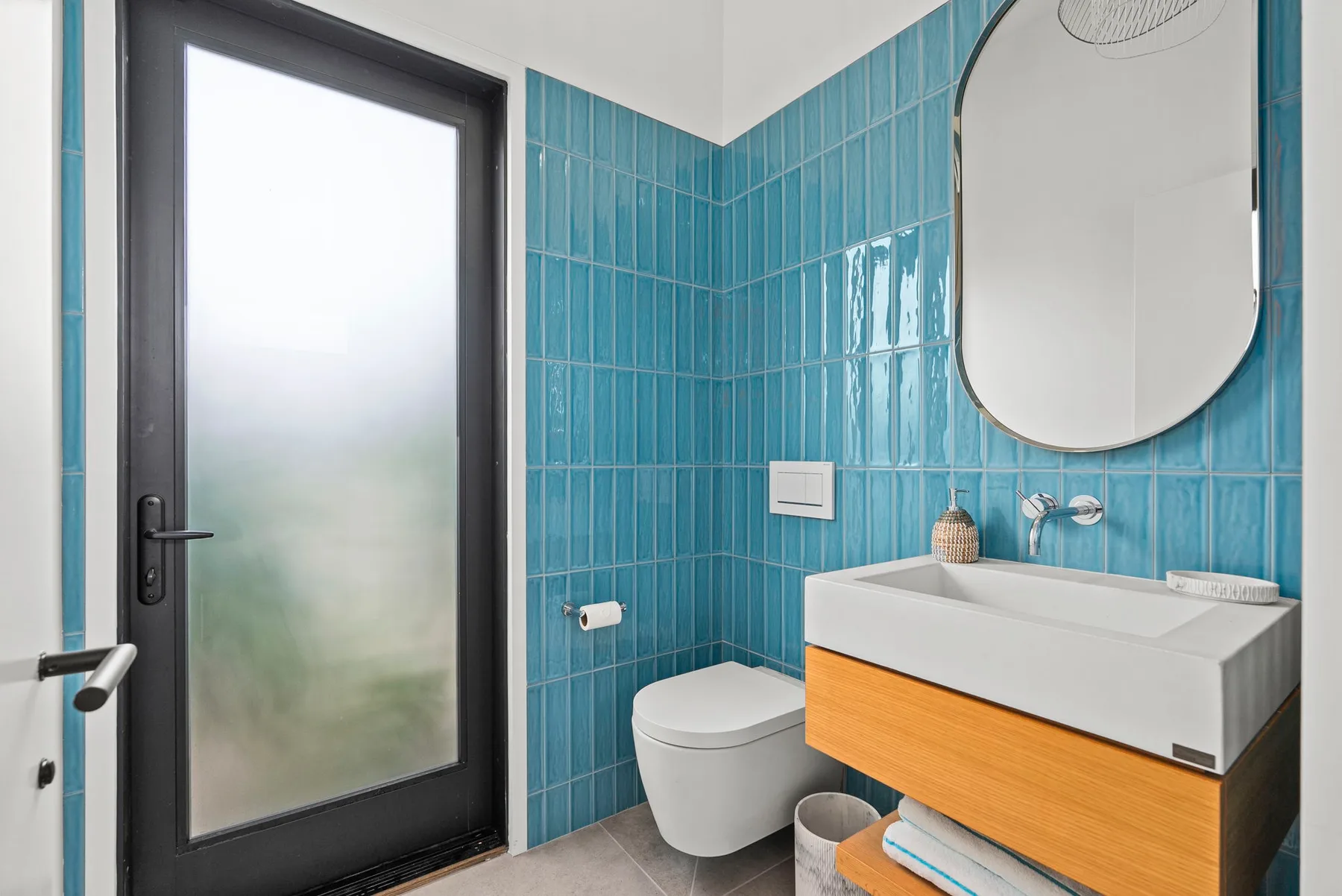 A bathroom with a white vanity, toilet, and blue tiled walls.