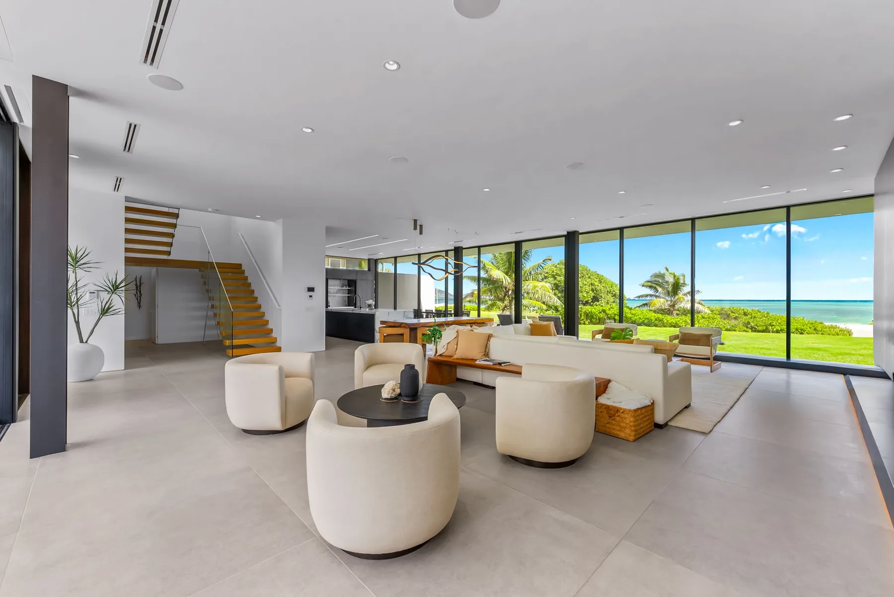 A bright living area with seating arranged beside floor-to-ceiling windows overlooking the ocean.