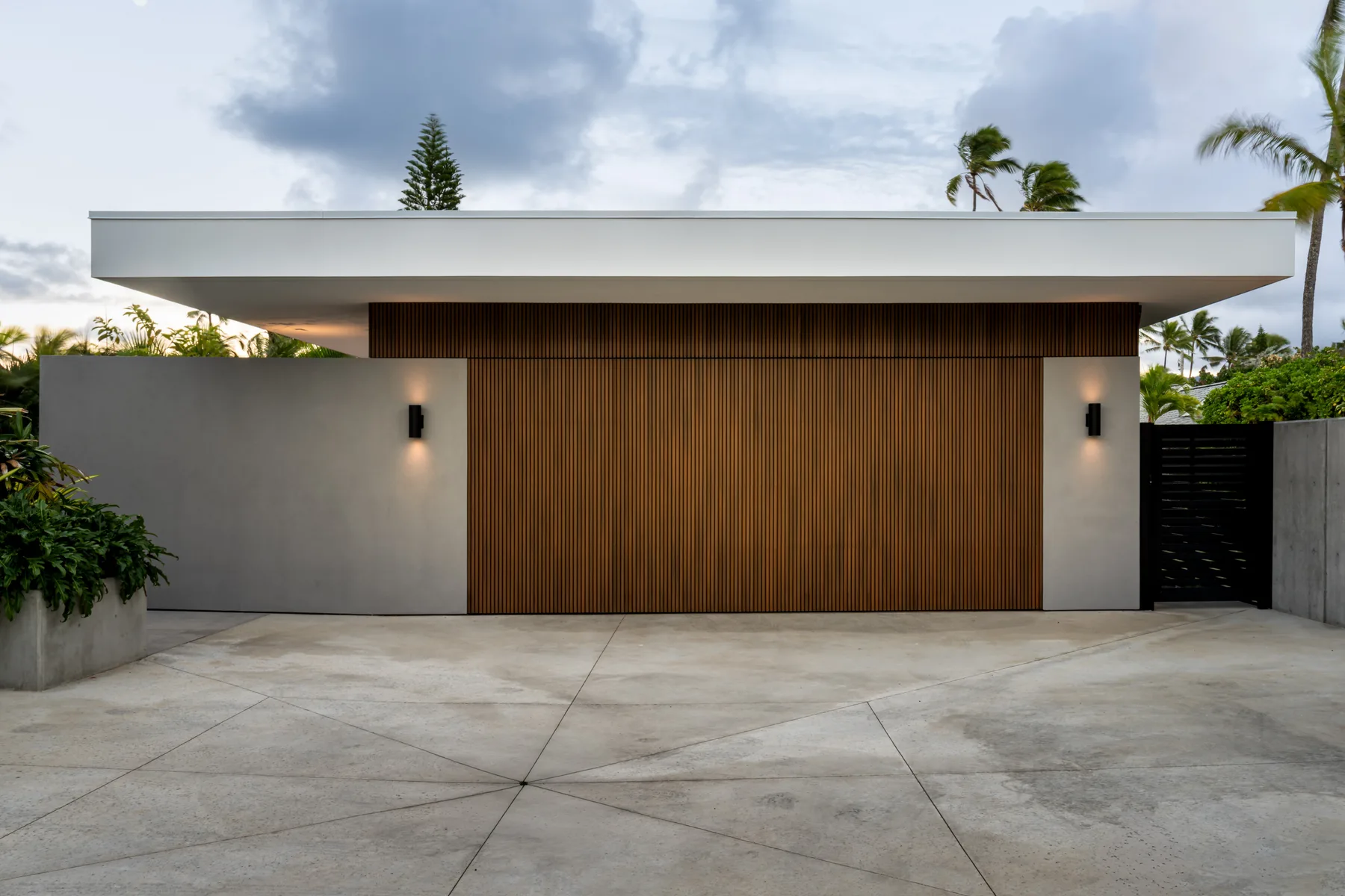 A modern house facade with a wide wooden gate and paved driveway.