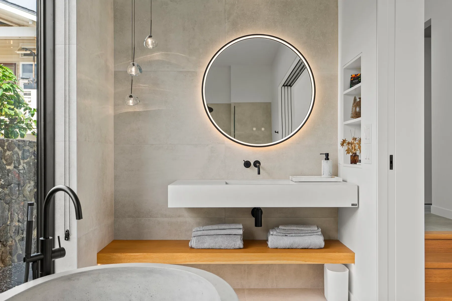 A modern bathroom features a wall-mounted sink and illuminated round mirror.