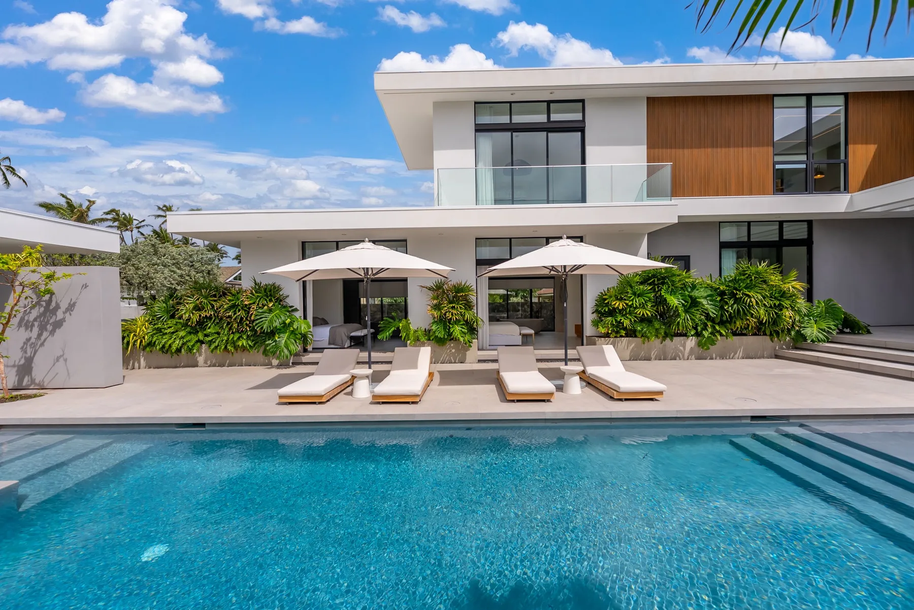 A modern house overlooks a swimming pool, with loungers and umbrellas along the patio.