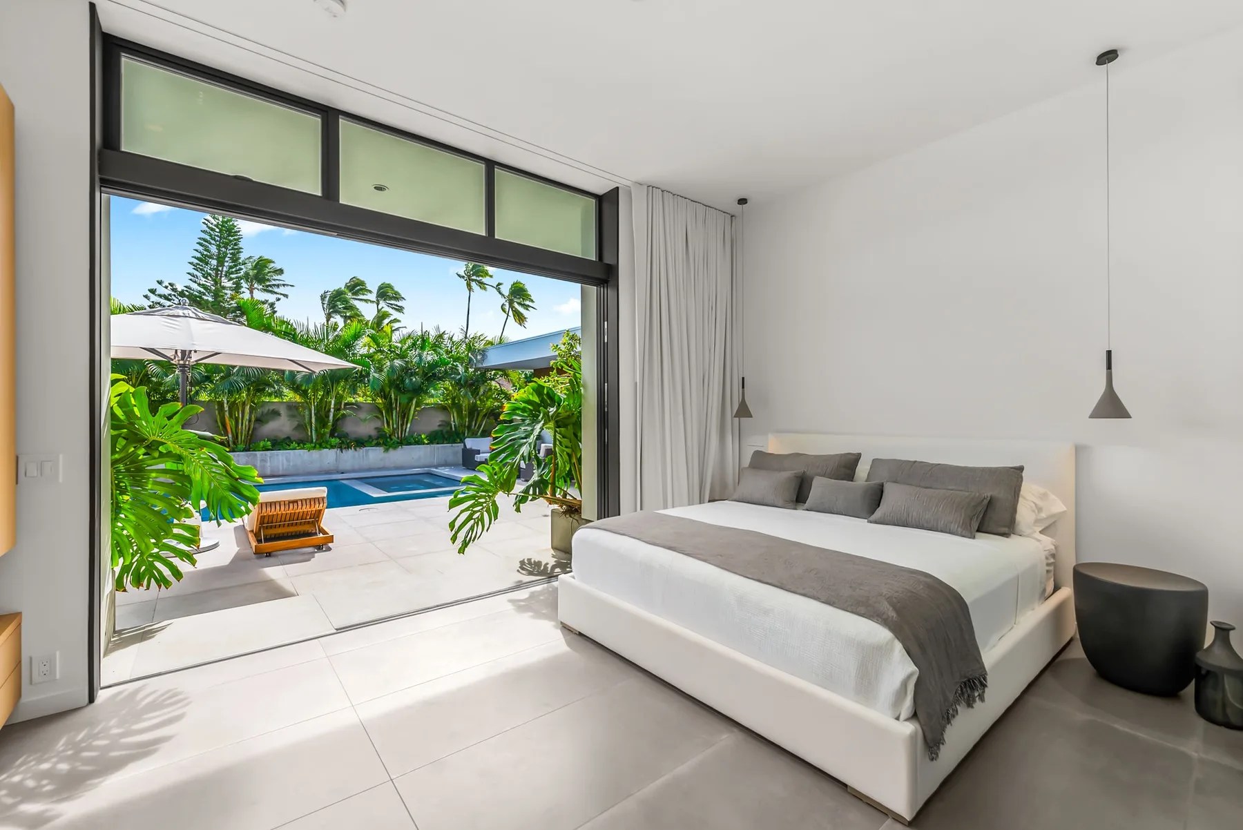 A bright bedroom opens onto a patio with a swimming pool and leafy plants.