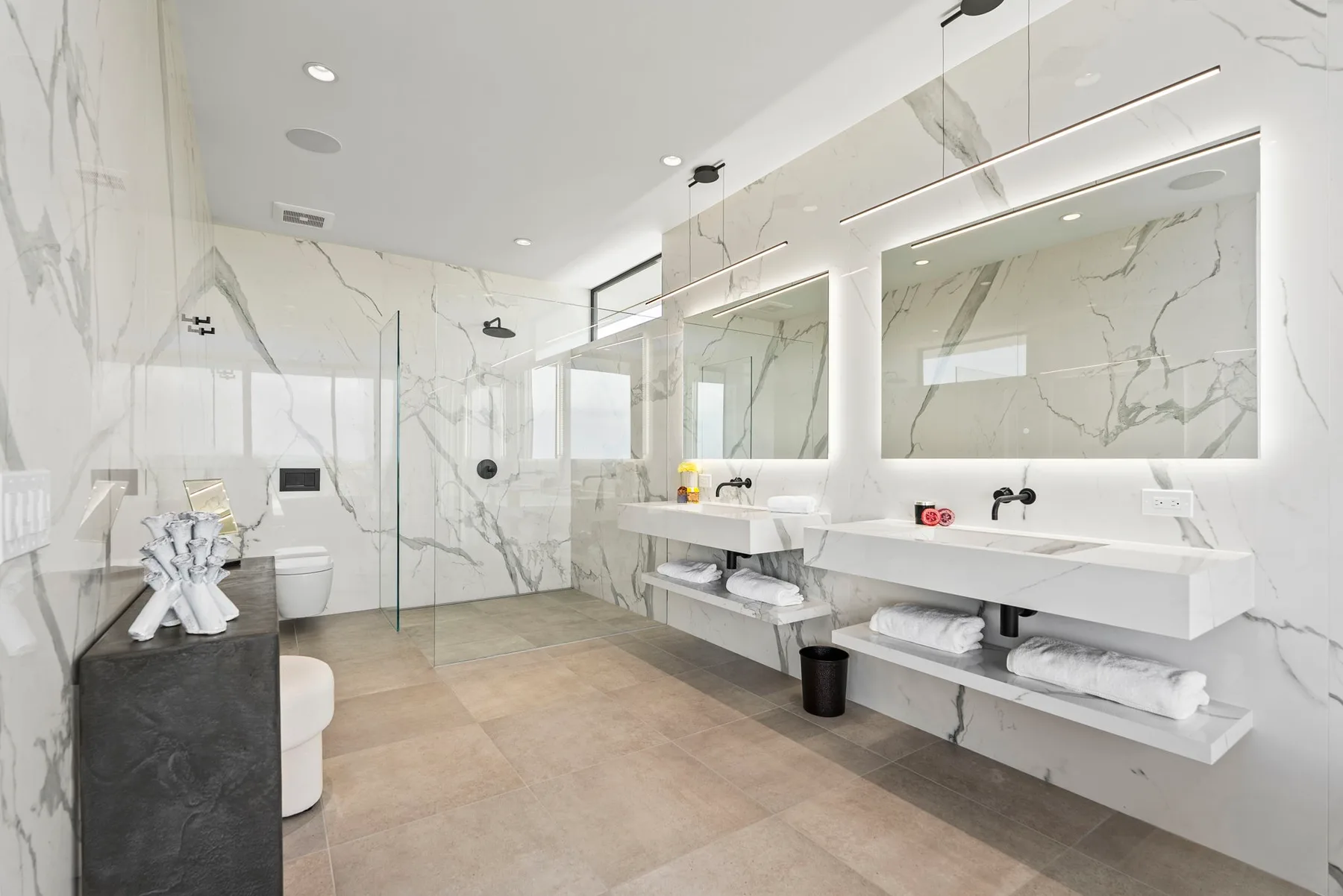 A bright bathroom with long sinks, large mirrors, and a glass shower.