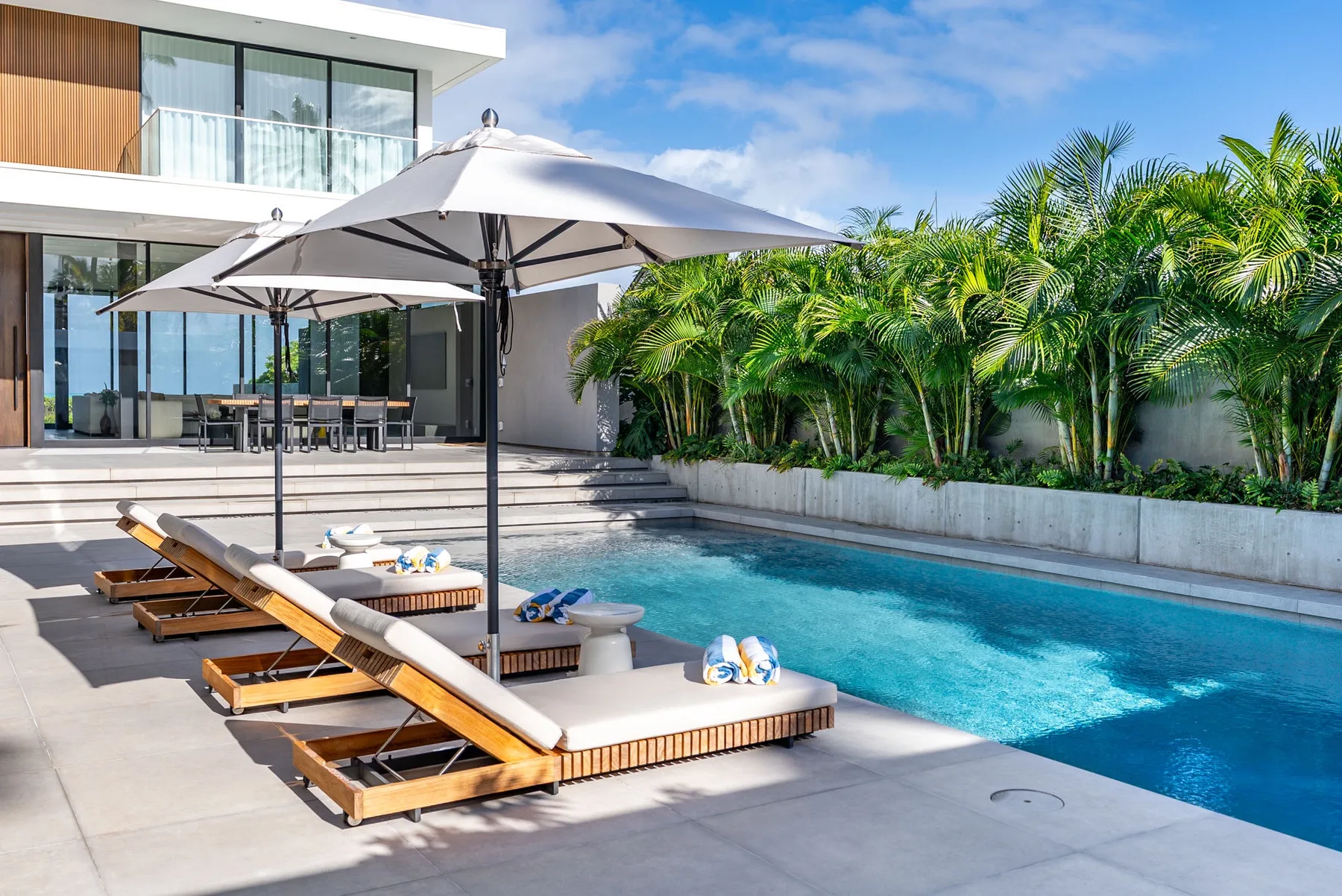A modern poolside patio with lounge seating and large umbrellas.