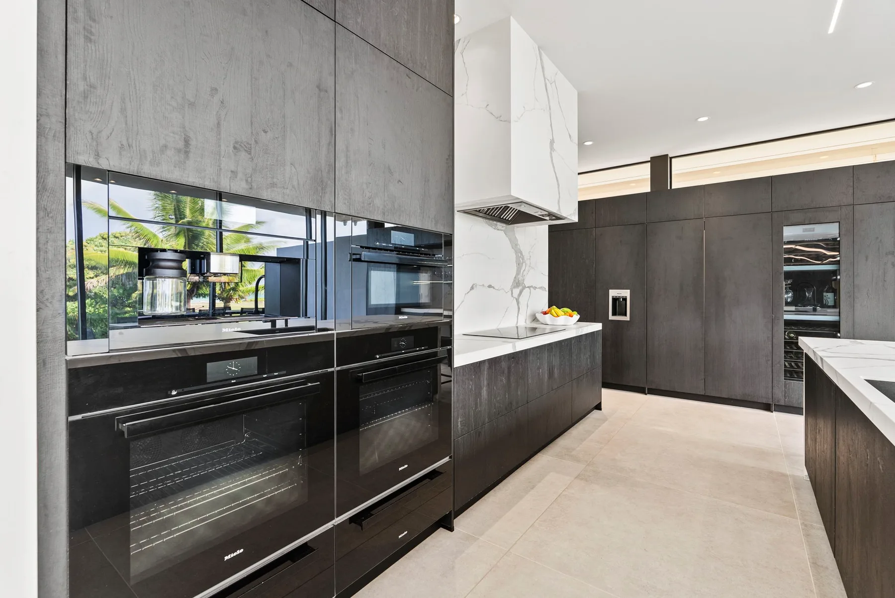 A modern kitchen with dark cabinetry, built-in ovens, and a central island.