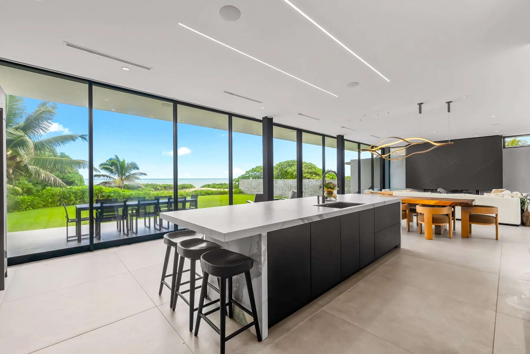 A modern kitchen with a large island and floor-to-ceiling windows overlooking greenery.