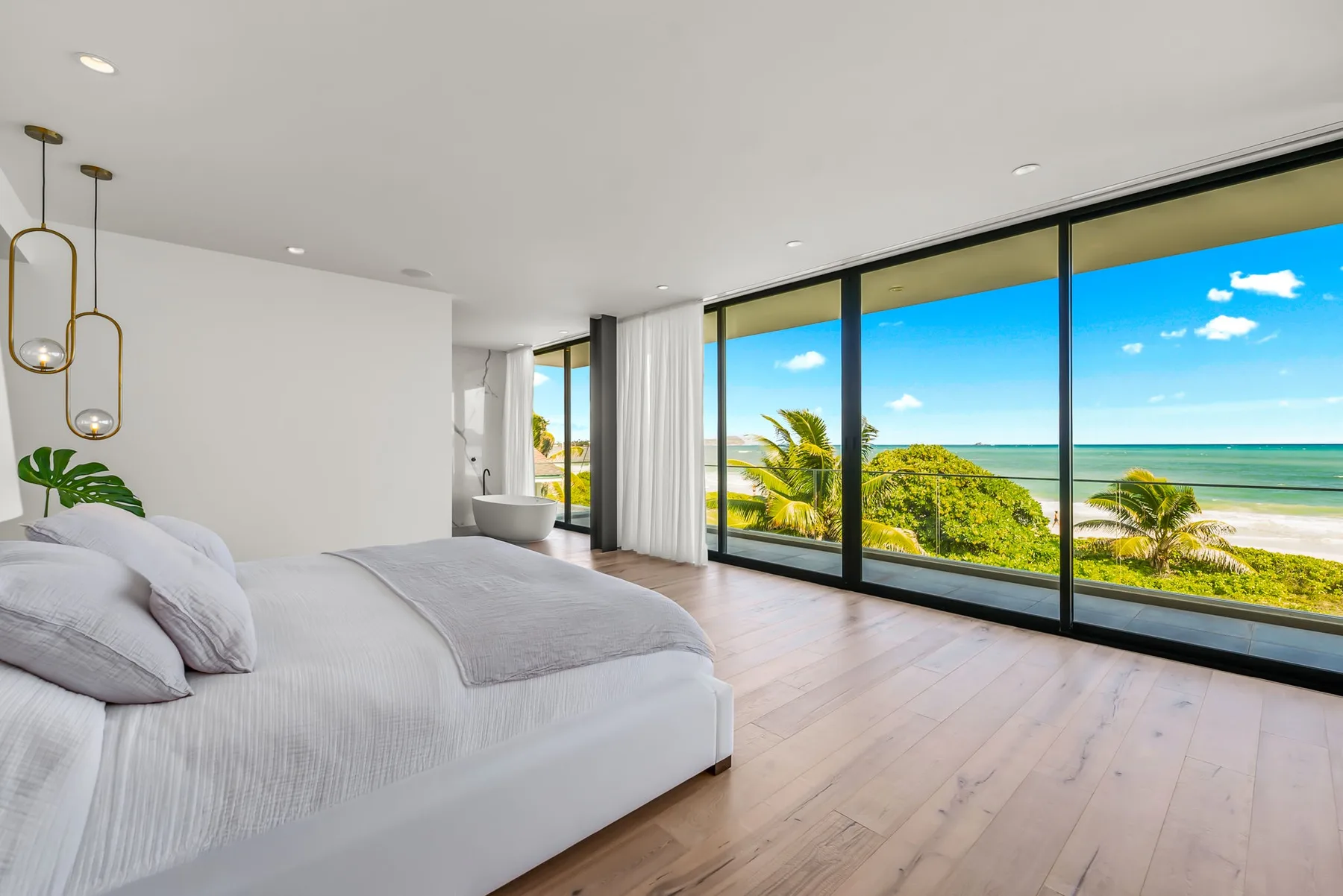 A bright bedroom opens onto expansive windows overlooking the ocean.