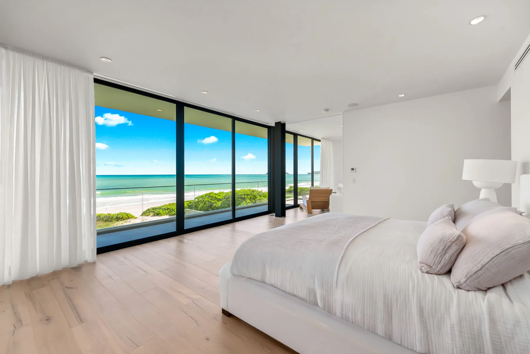 A bright bedroom with a bed beside large windows overlooking the beach.