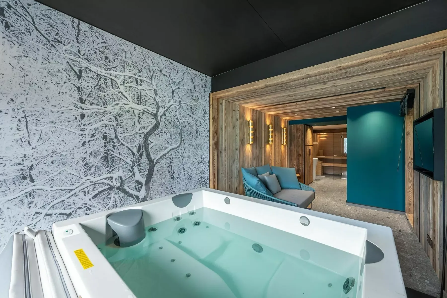 A whirlpool tub sits beside a blue-gray winter tree mural and a teal door.