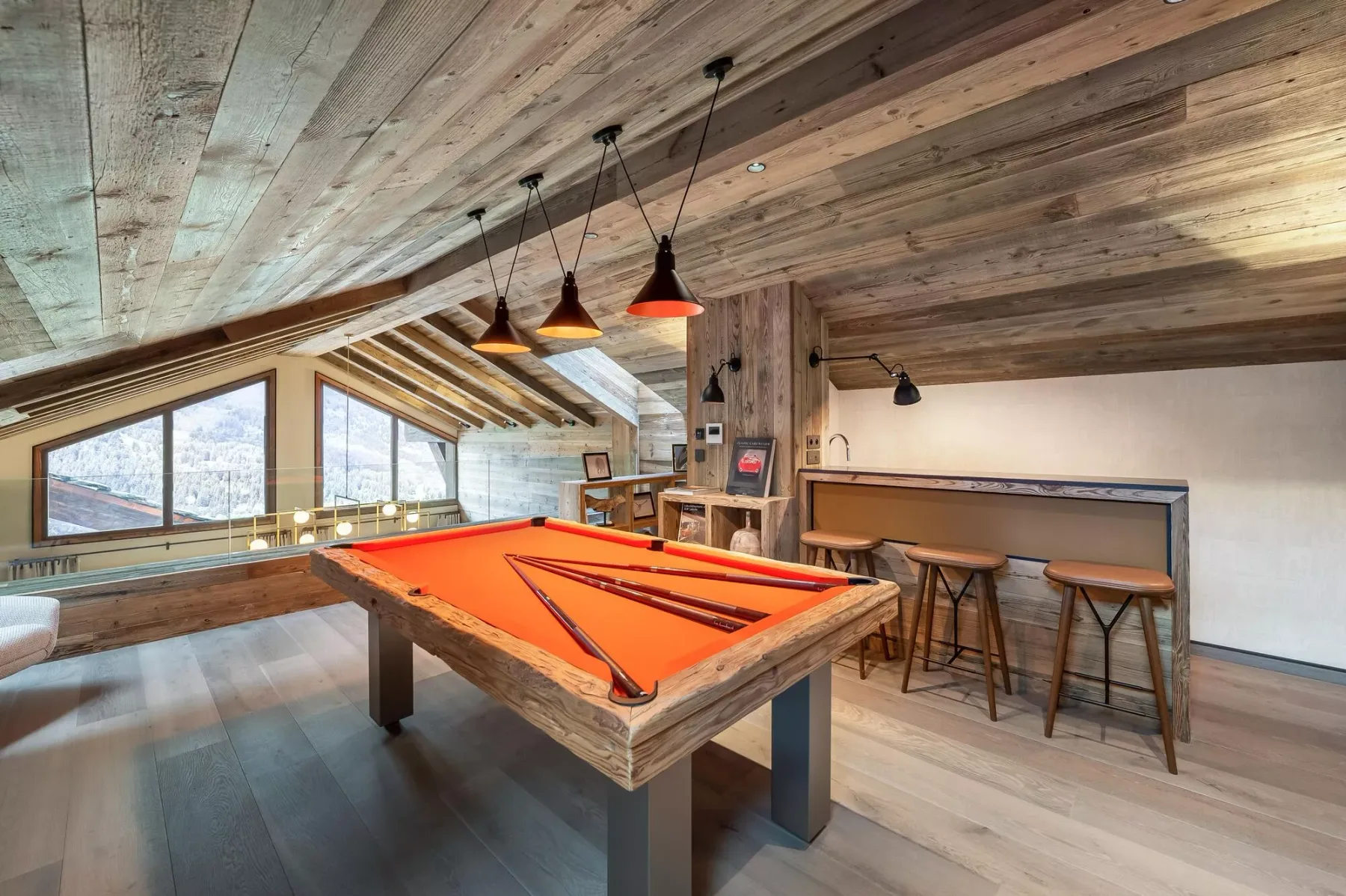 A game room with a pool table, hanging lights, and a counter with stools.