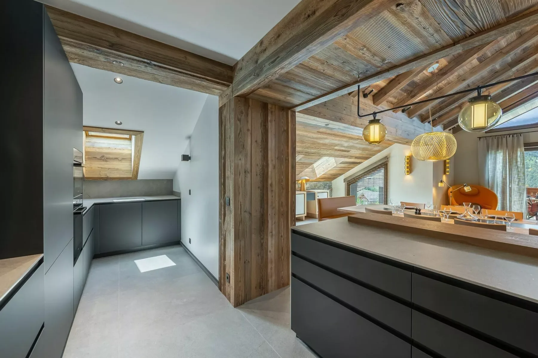 A modern kitchen with dark cabinets, a wide island, and exposed timber beams.