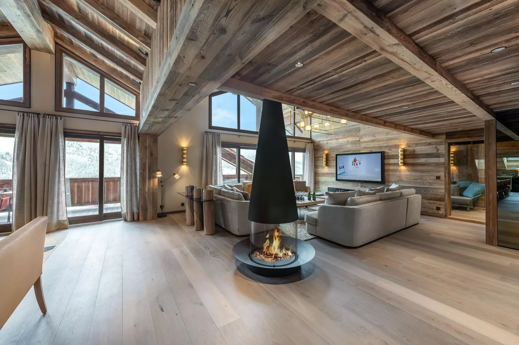 A spacious living room with a suspended fireplace and seating beneath a timber ceiling.