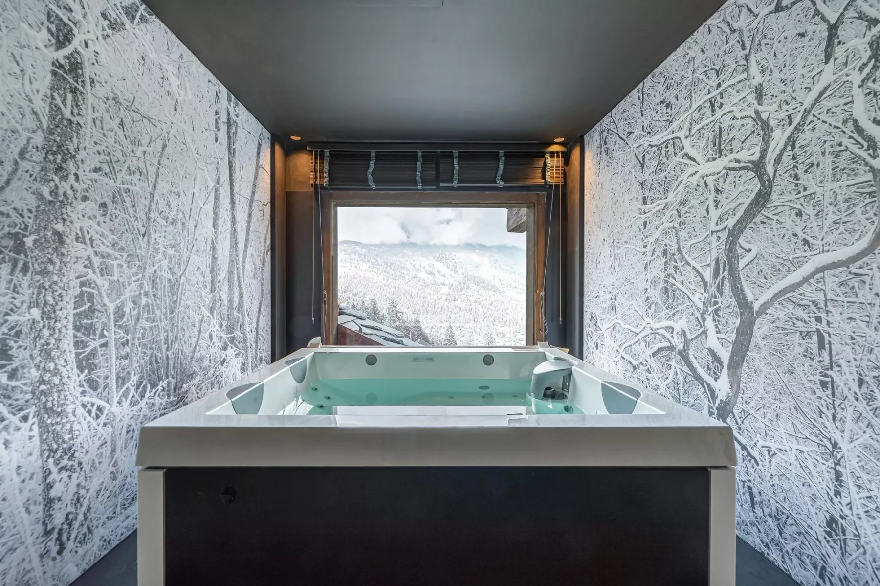 A hot tub sits in a room with winter forest murals and a large window.