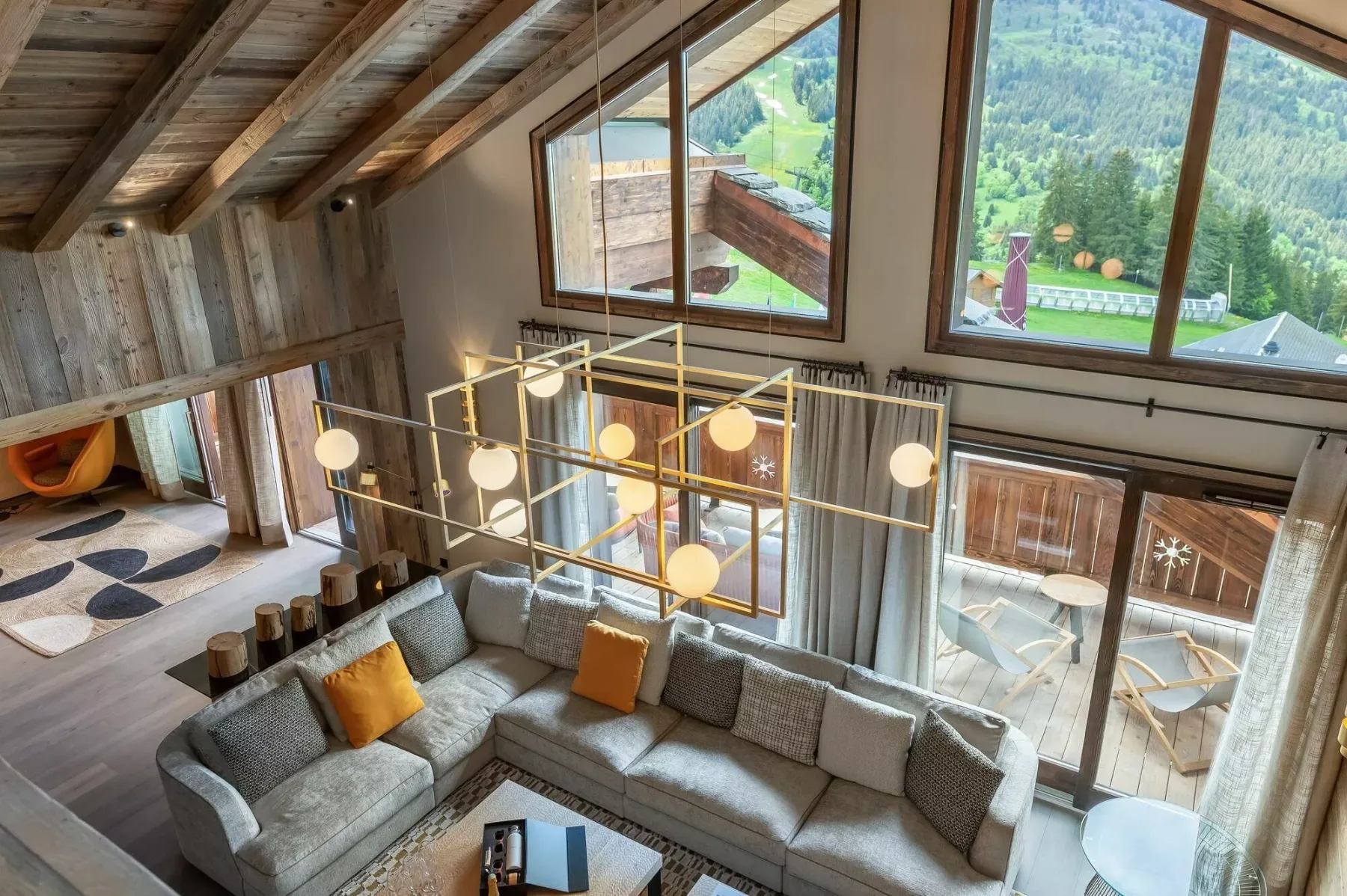 A loft living room with sectional seating beneath sloped timber ceilings and large windows.