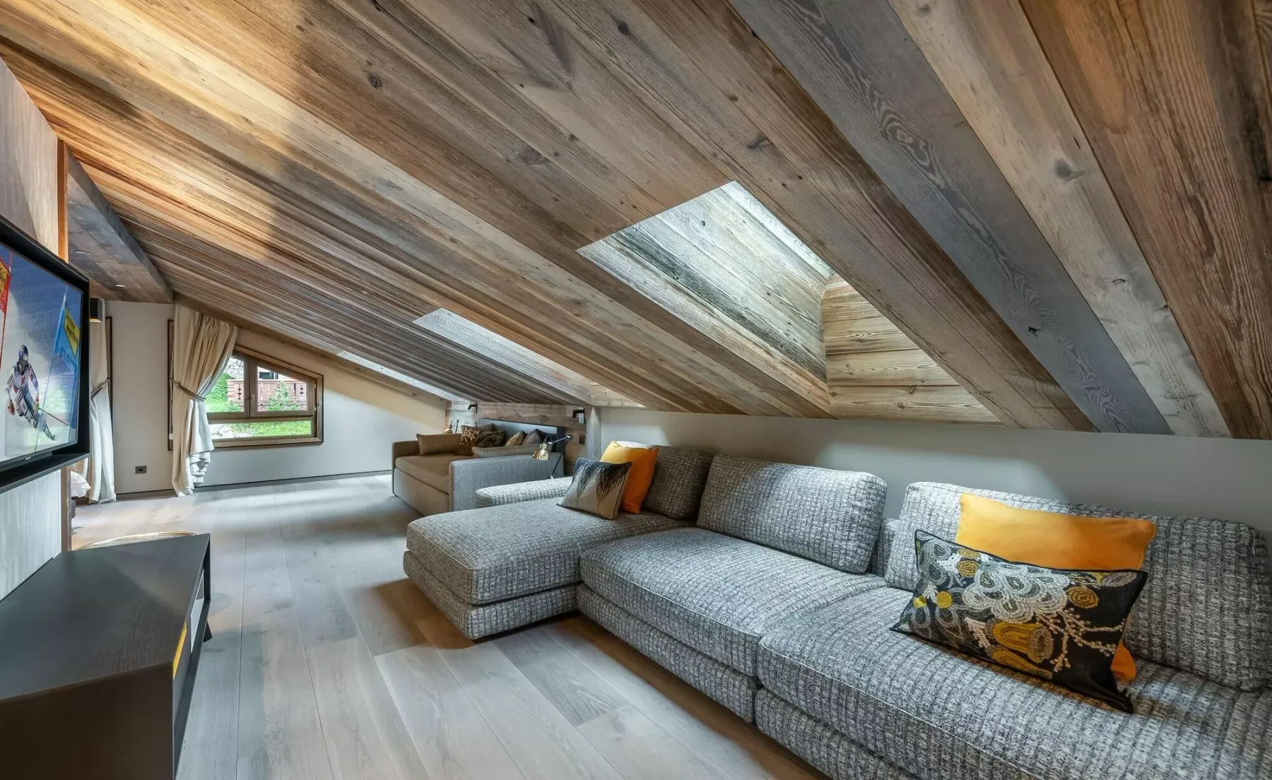 A living room with sectional seating beneath a sloped wood ceiling and skylight.
