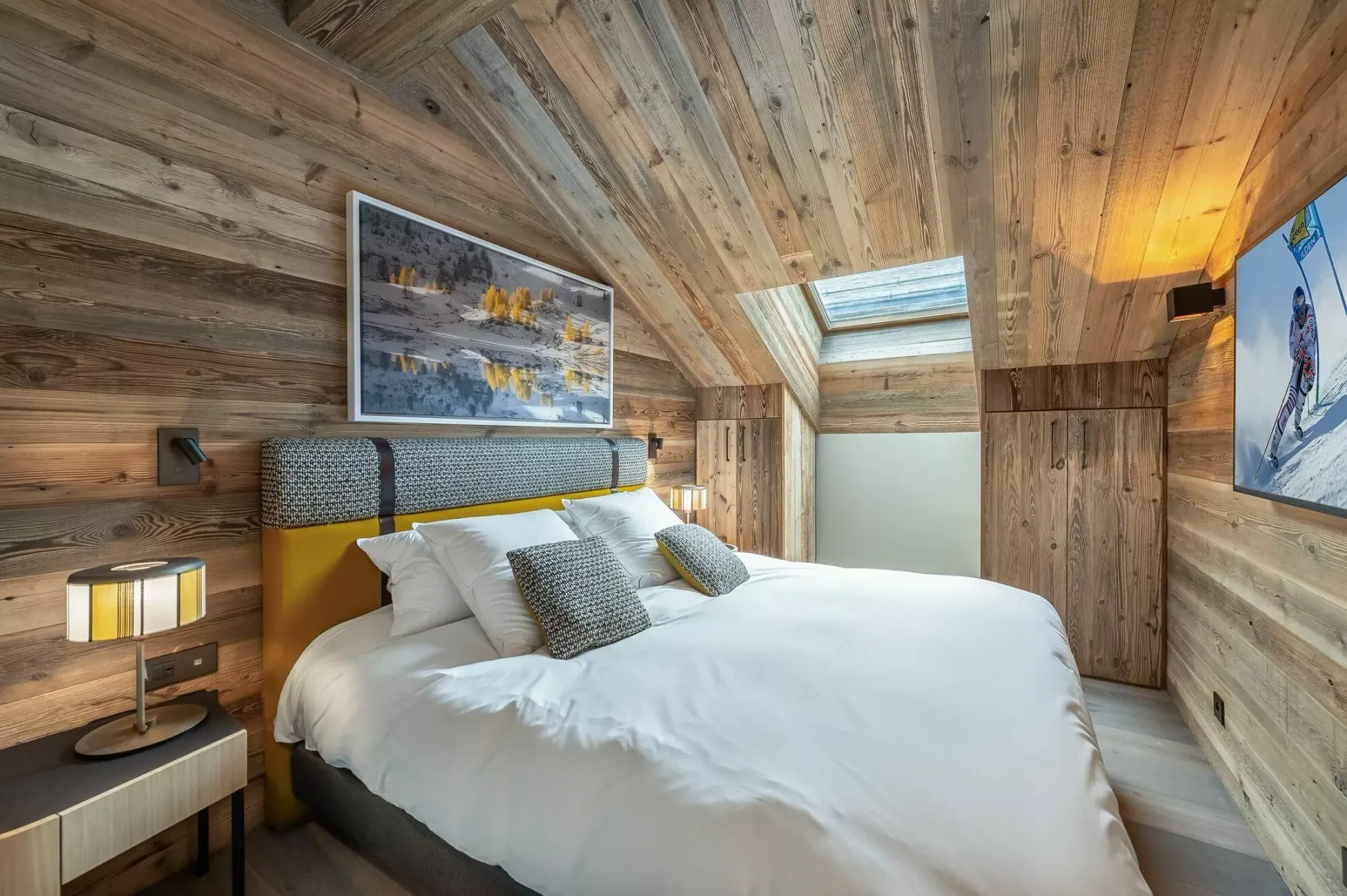 A bedroom with a large bed beneath a sloped wood-paneled ceiling.