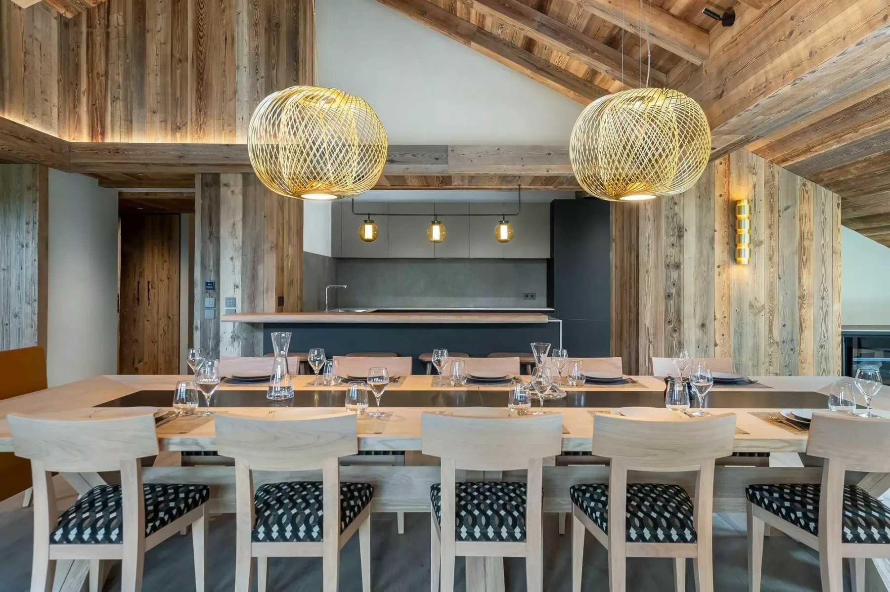 A dining area with a long set table and woven pendant lights beneath a wooden ceiling.