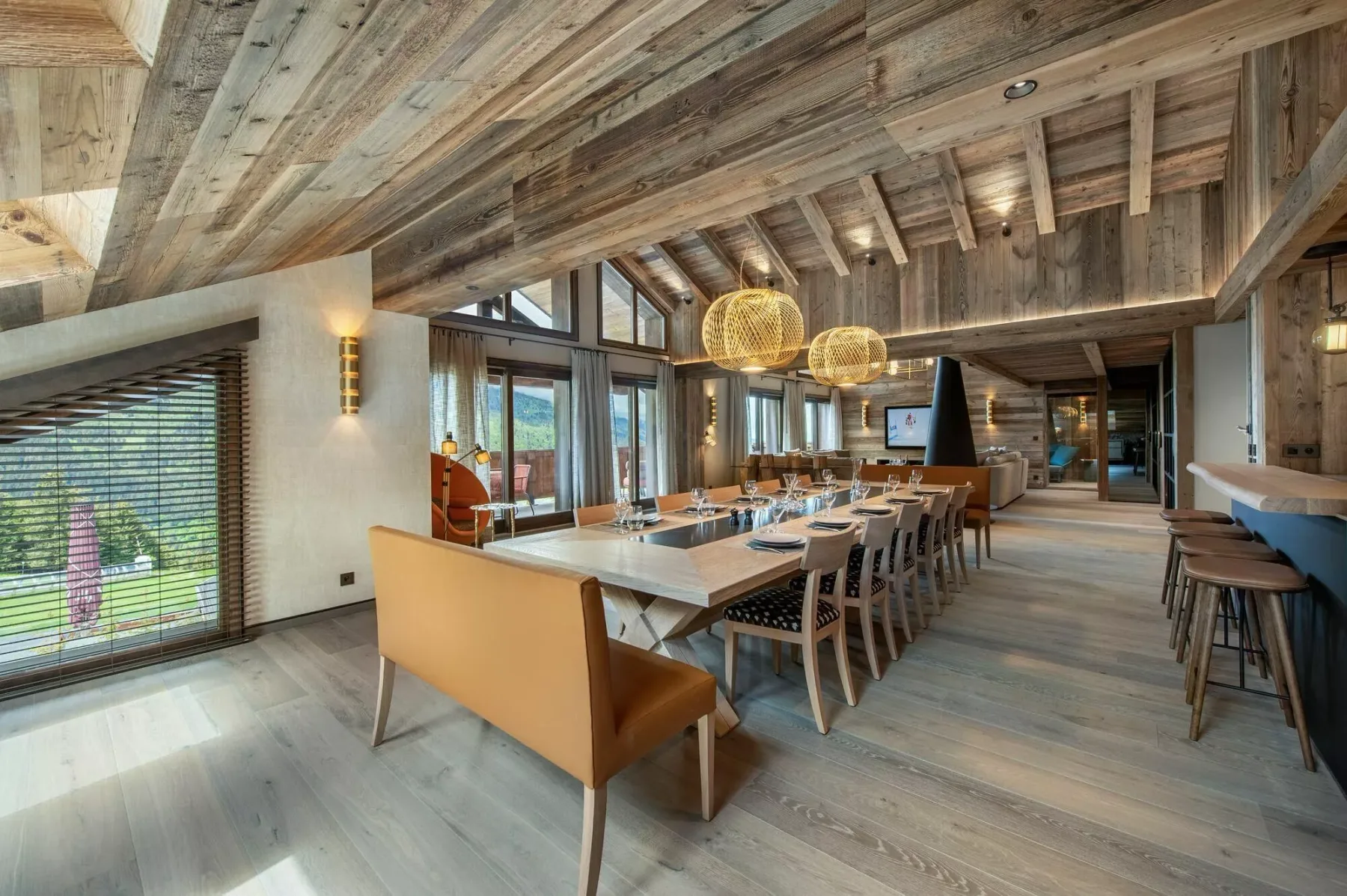 A dining area with a long table, seating, and large windows beneath a timber ceiling.