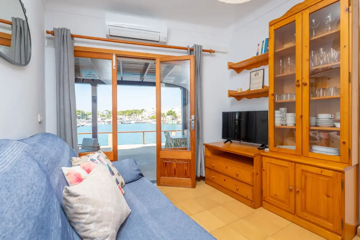 Una sala de estar con asientos azules, muebles de madera y puertas de cristal con vistas al agua.