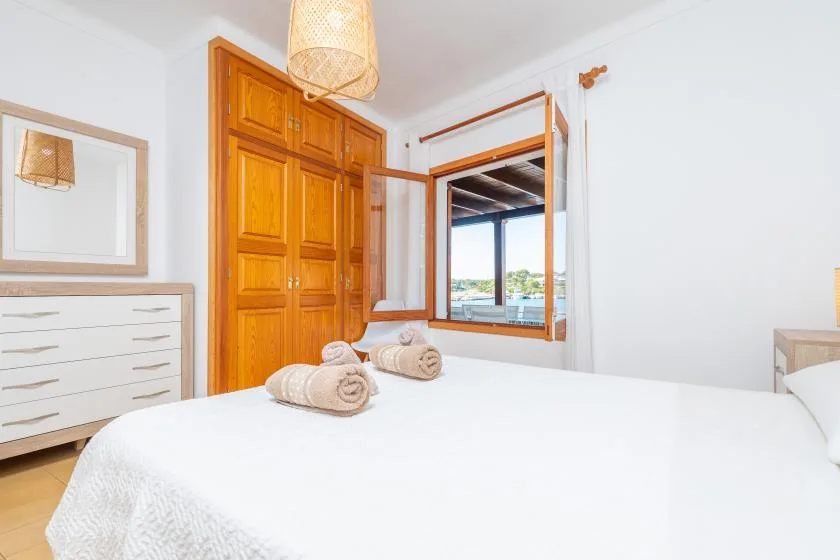 Un dormitorio con una cama blanca, un armario de madera y una ventana abierta.